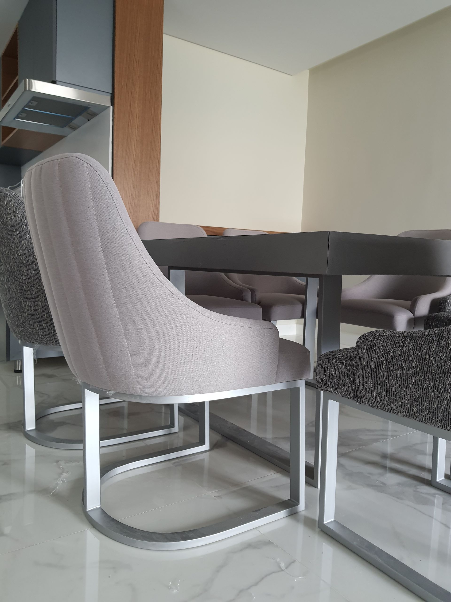 A light gray upholstered chair with a chrome base is set at a dark gray table in a well-lit room.