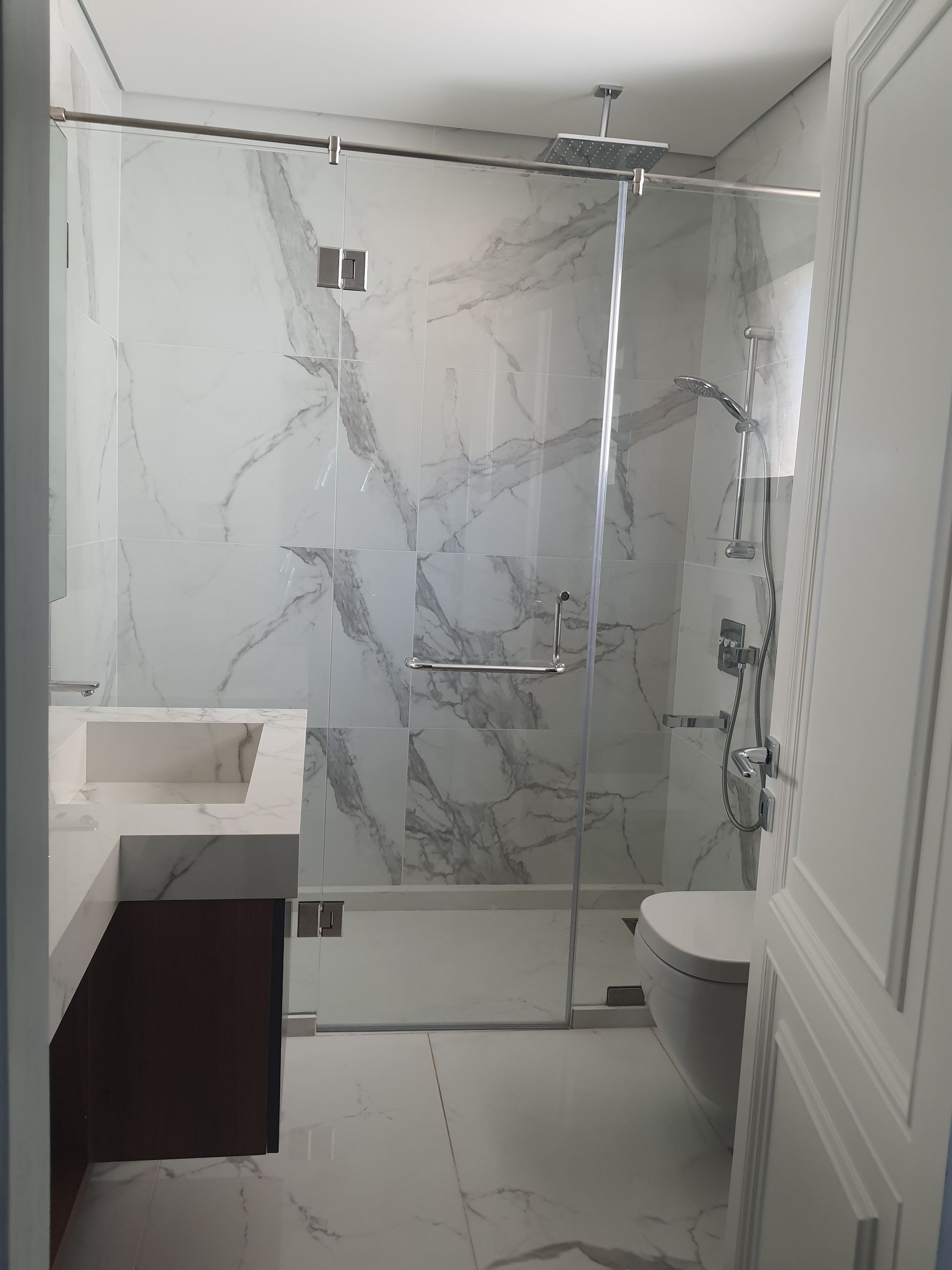 Modern bathroom with marble tiles, glass shower, and a white toilet.