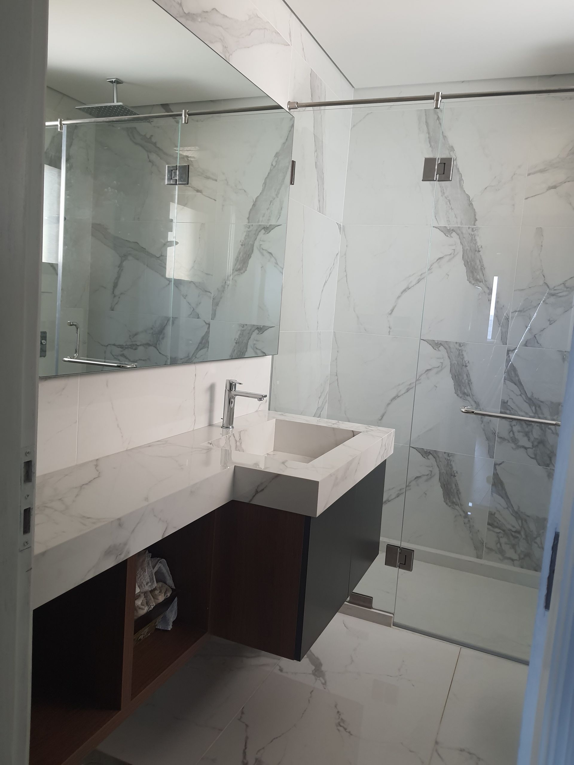 Modern bathroom with marble-look walls, glass shower enclosure, floating vanity, and large mirror.