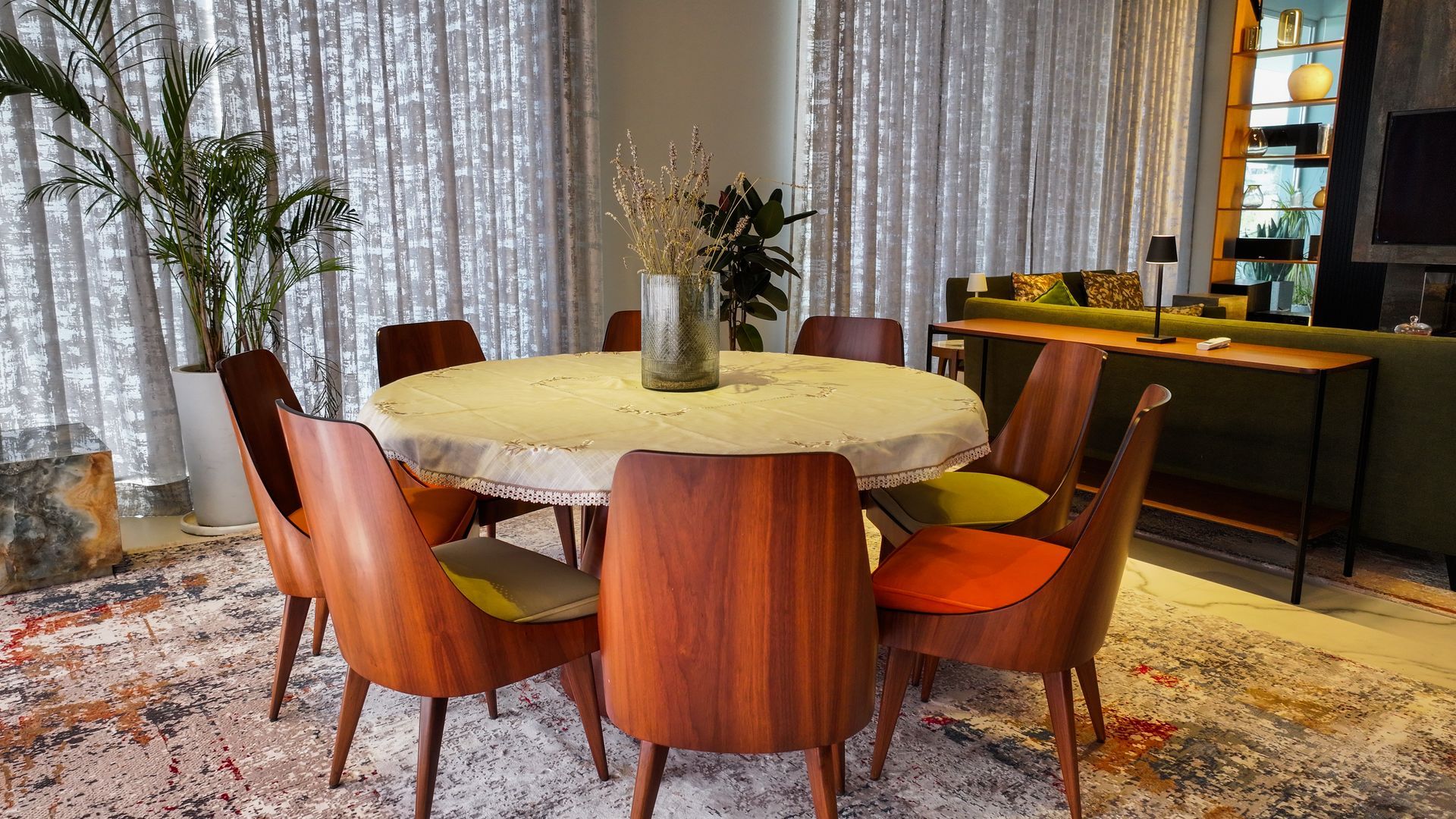 Dining room: wooden table, chairs, plants, rug, window with curtains.