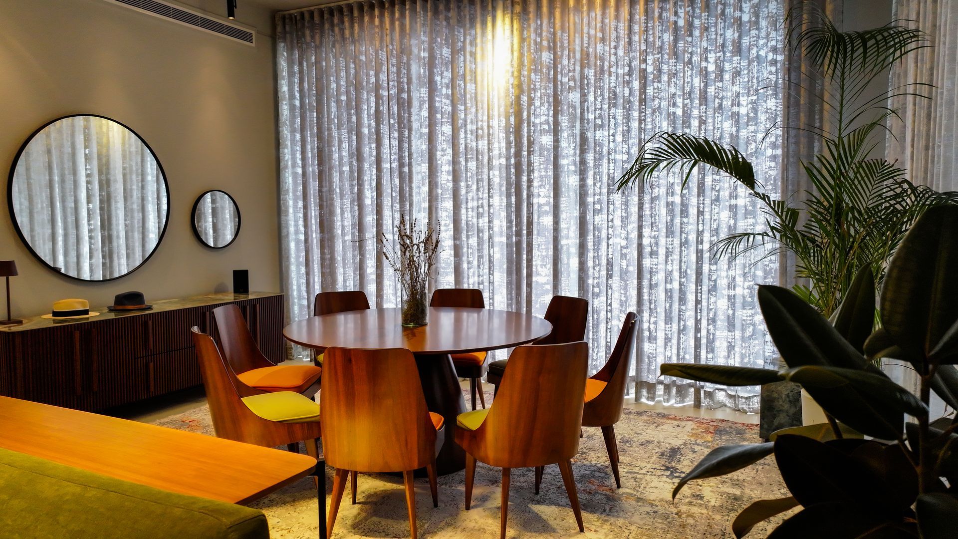 Dining room with round wooden table, chairs, large curtains, and mirrors.