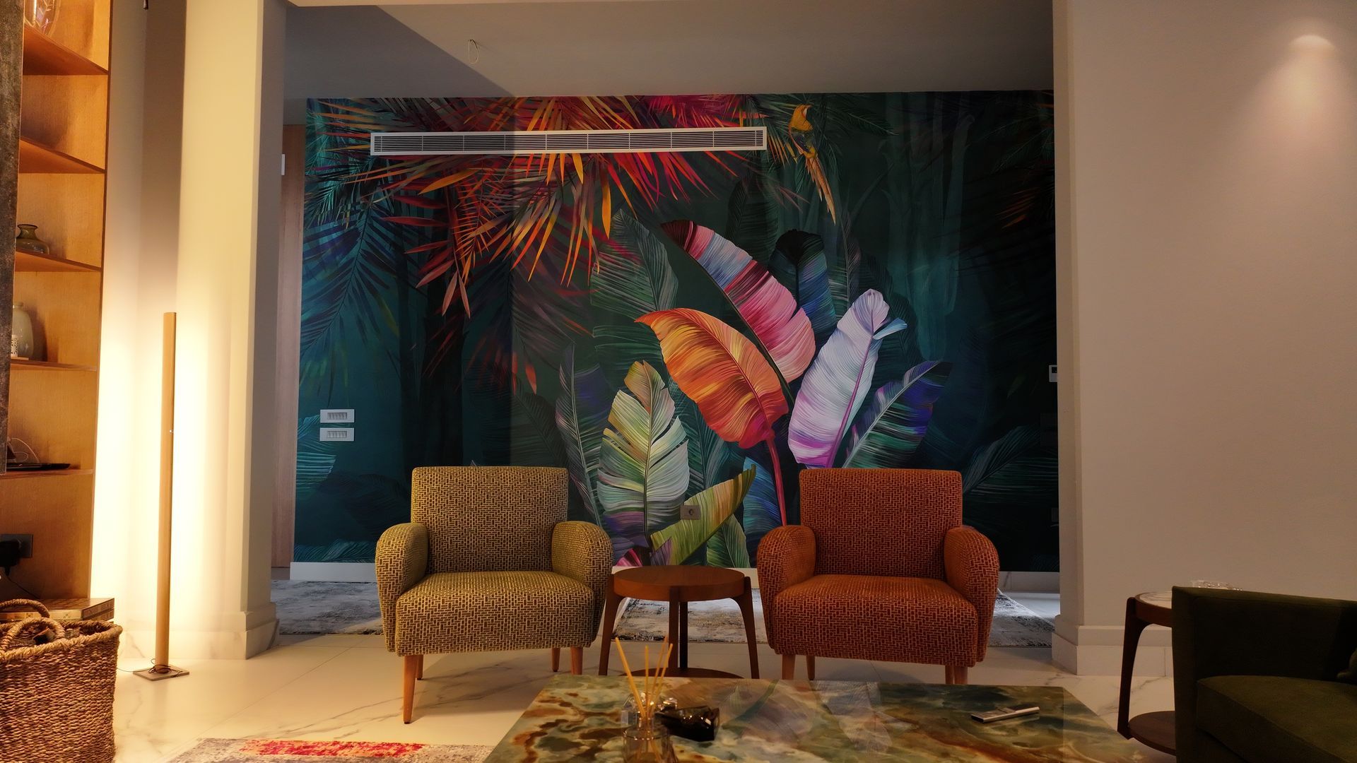 Two armchairs facing jungle mural, small table. White walls, floor, and tall lamp.