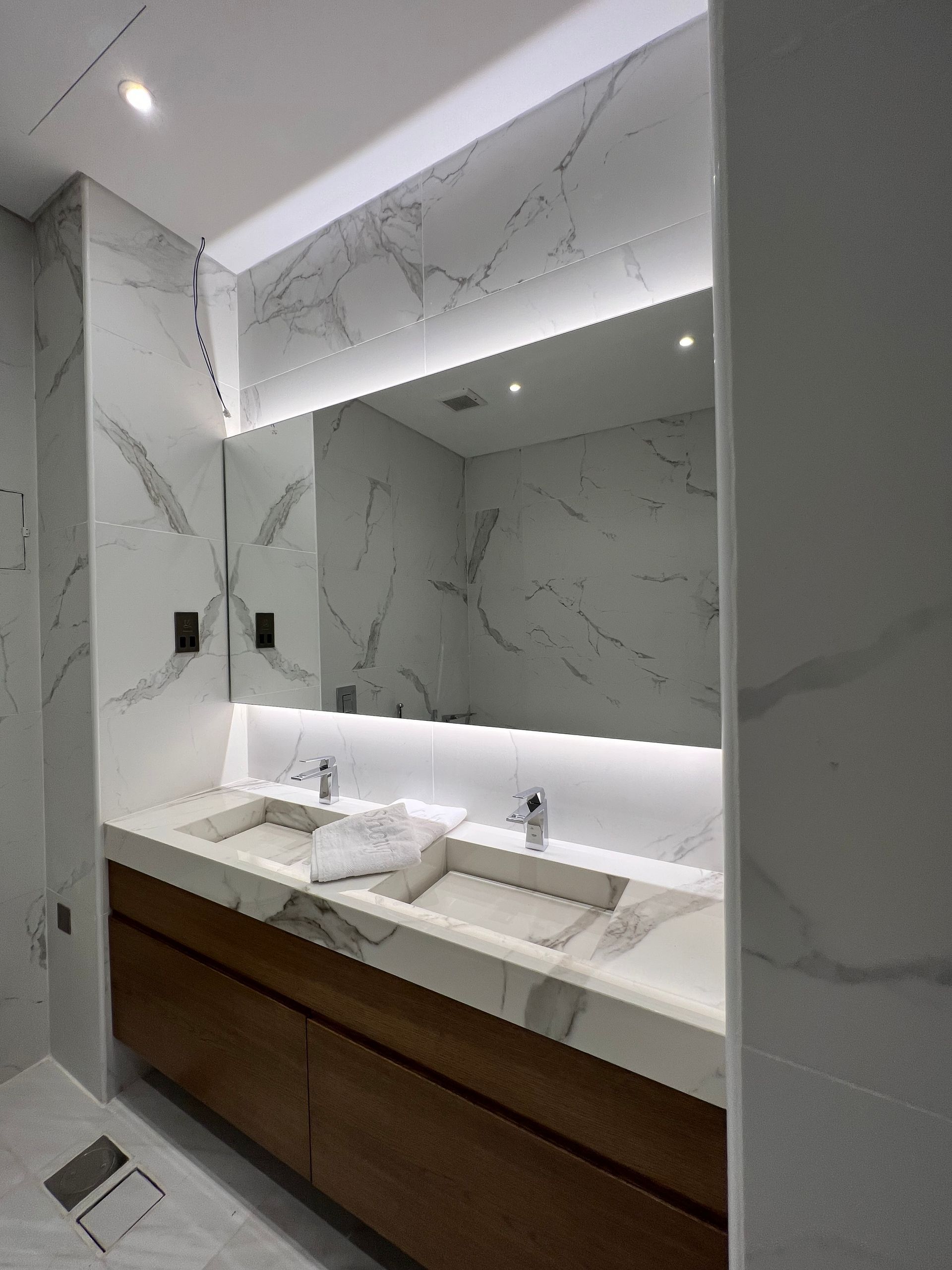 Modern bathroom with marble walls, a wooden vanity, and a large mirror with integrated lighting.
