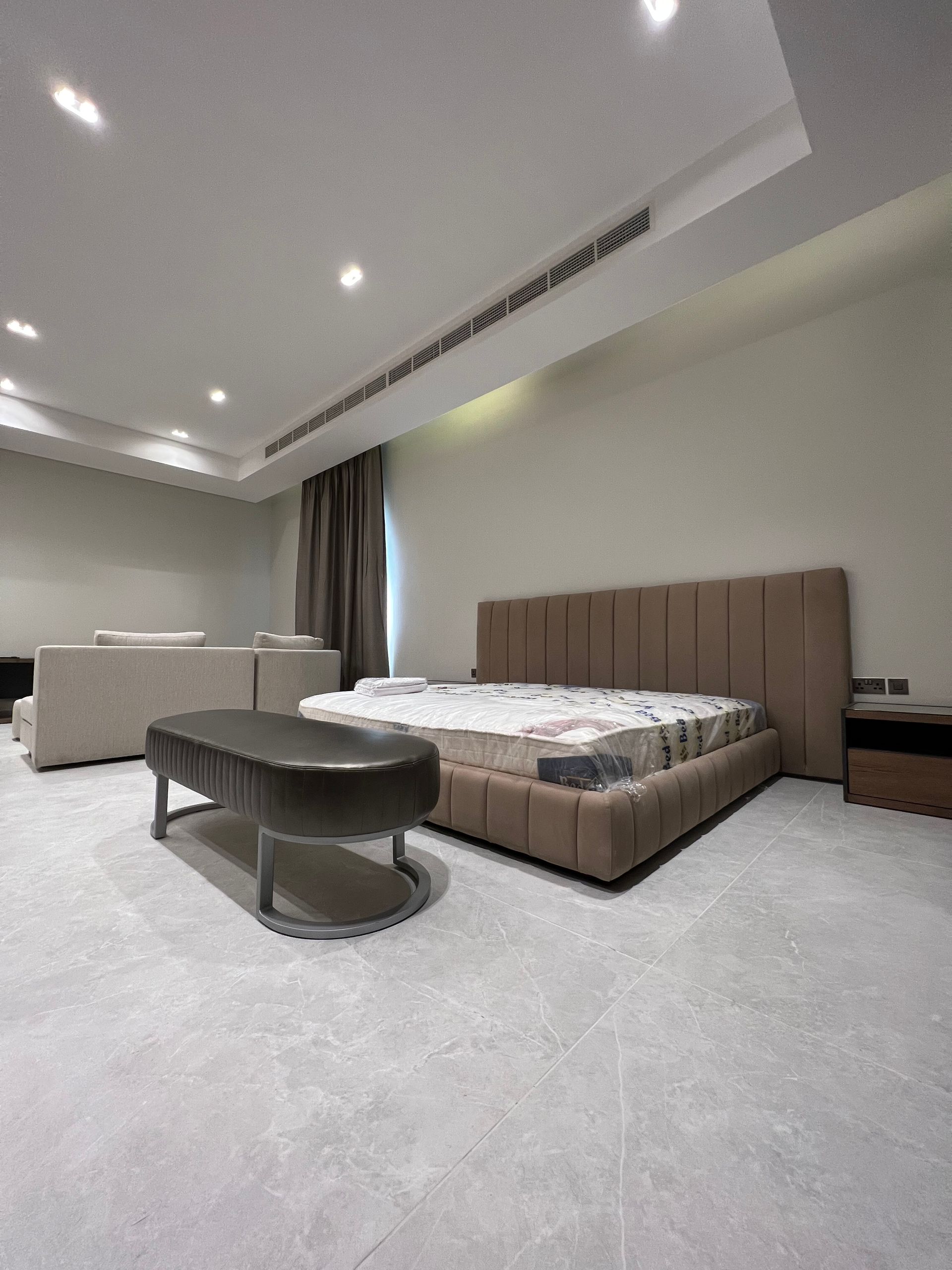 Bedroom with a beige bed, a gray bench, and gray flooring.