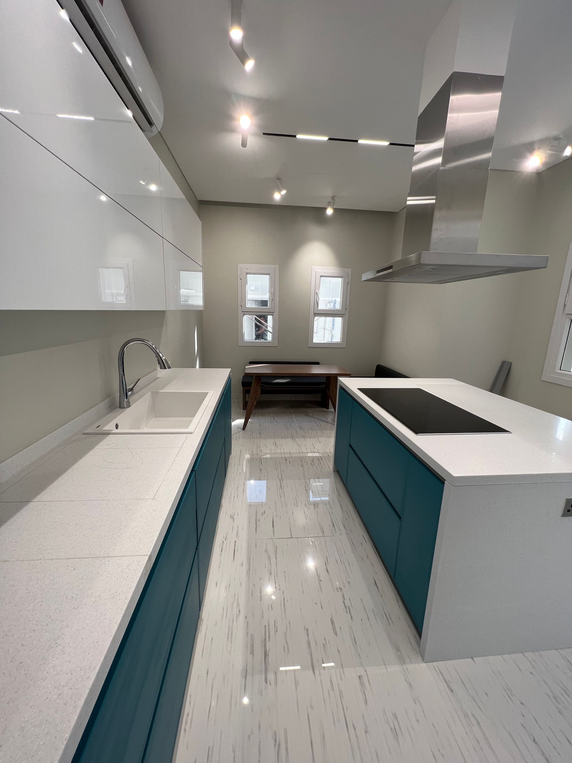 Modern kitchen with teal cabinets, white countertops, stainless steel range hood.