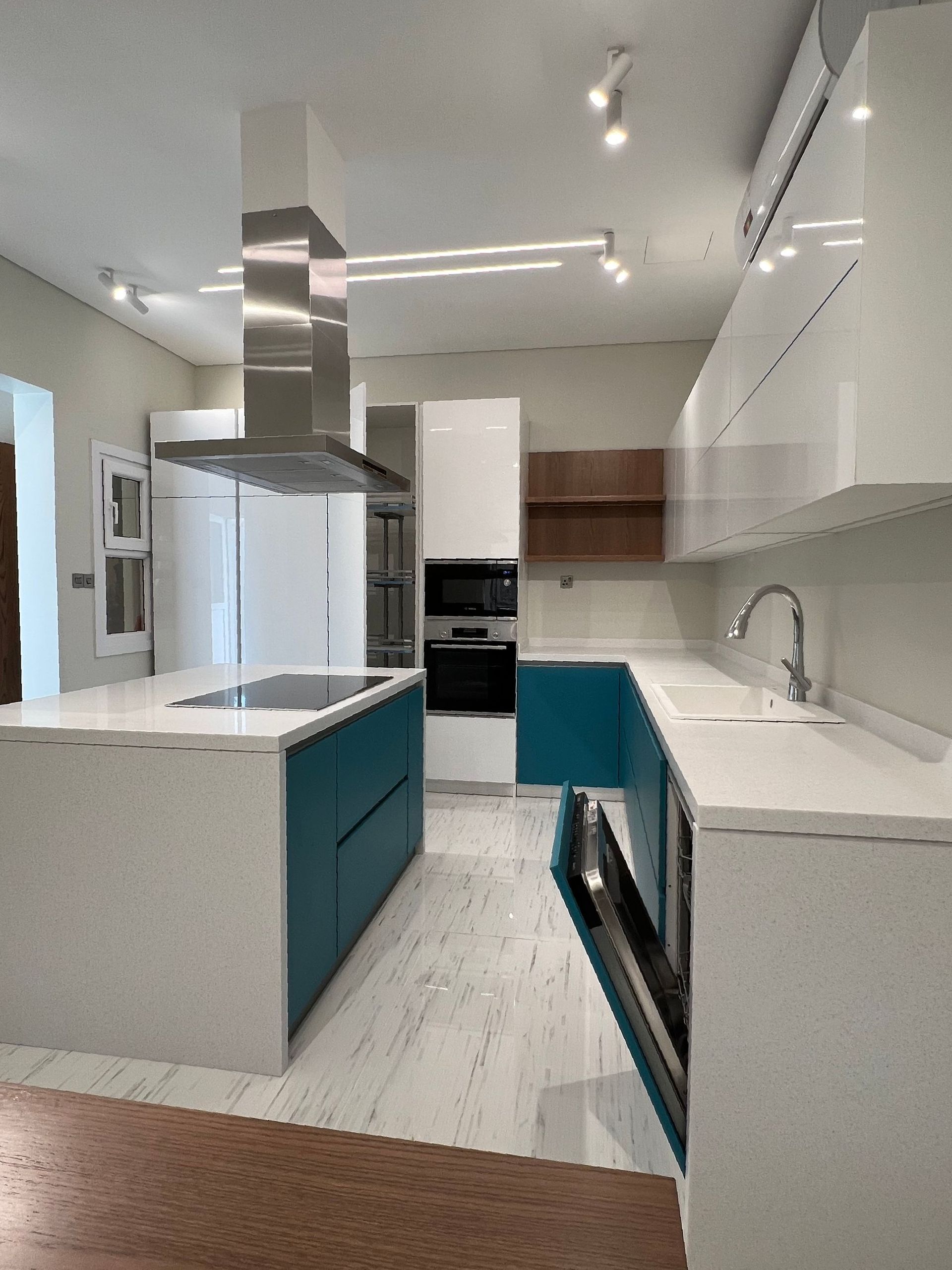 Modern kitchen with white cabinets, teal accents, stainless steel hood, and island.