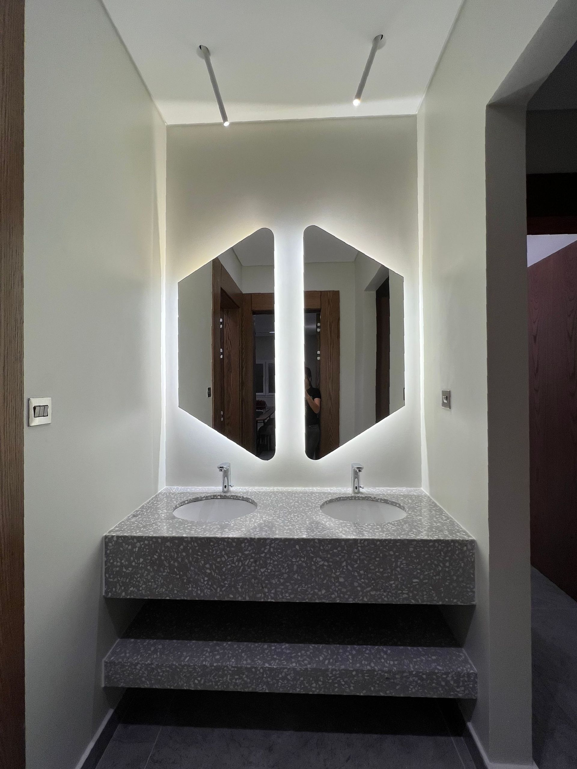 Bathroom with two sinks, unique mirror, and terrazzo countertop. Grey walls and dark flooring.