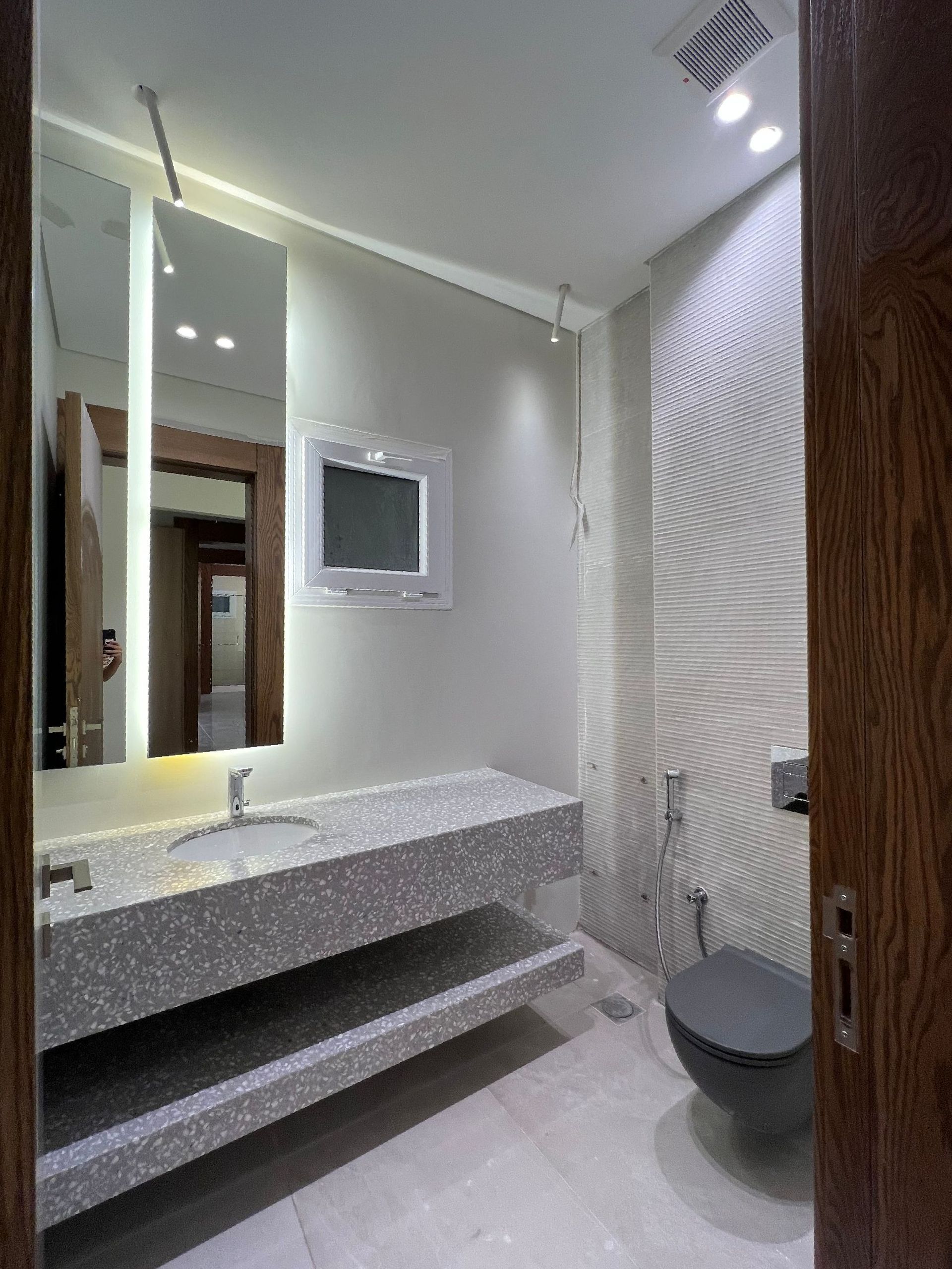 Modern bathroom with gray stone vanity, toilet, and textured wall.