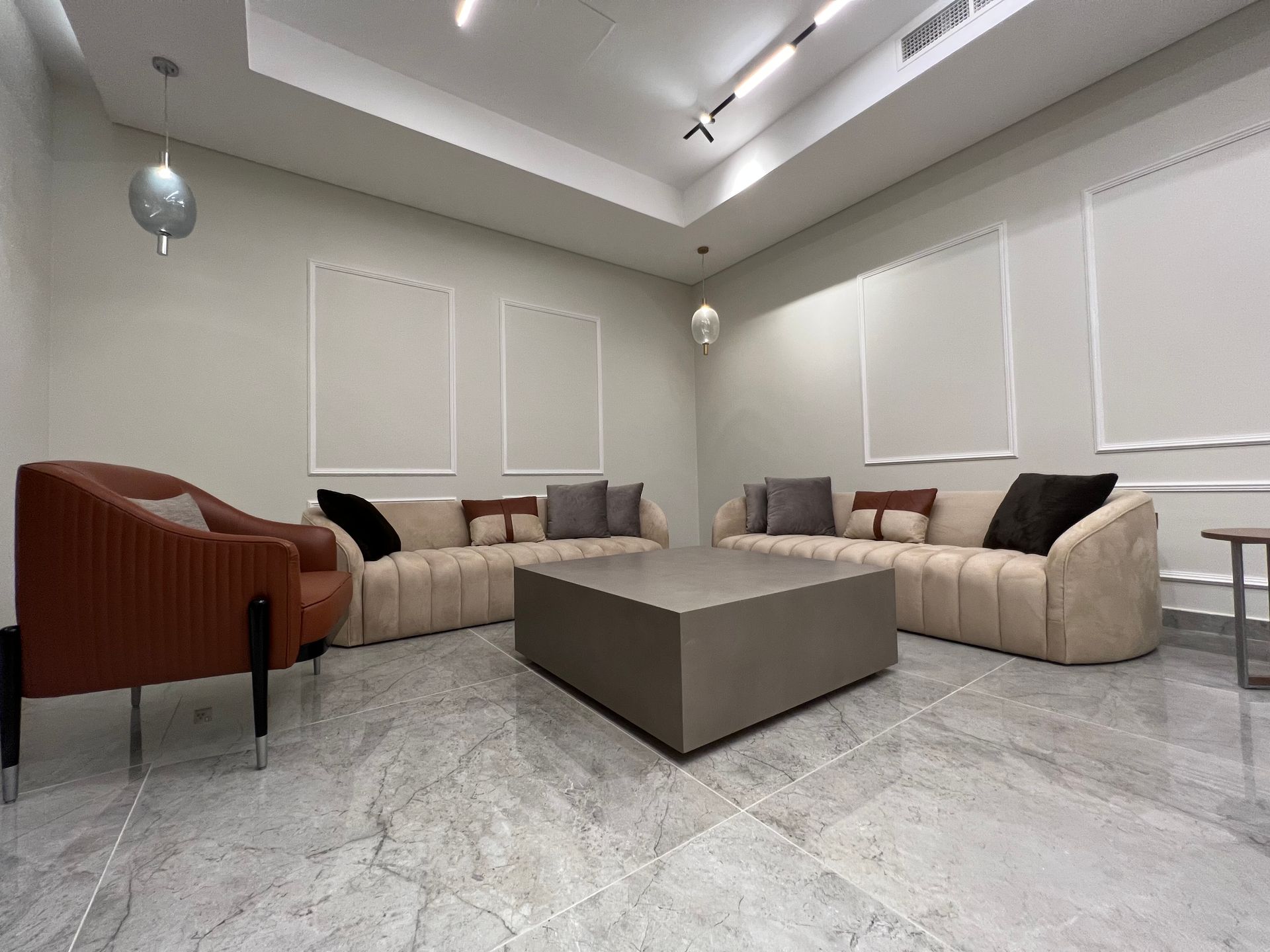A modern living room with beige sofas, a brown chair, and a gray coffee table on a marble floor.