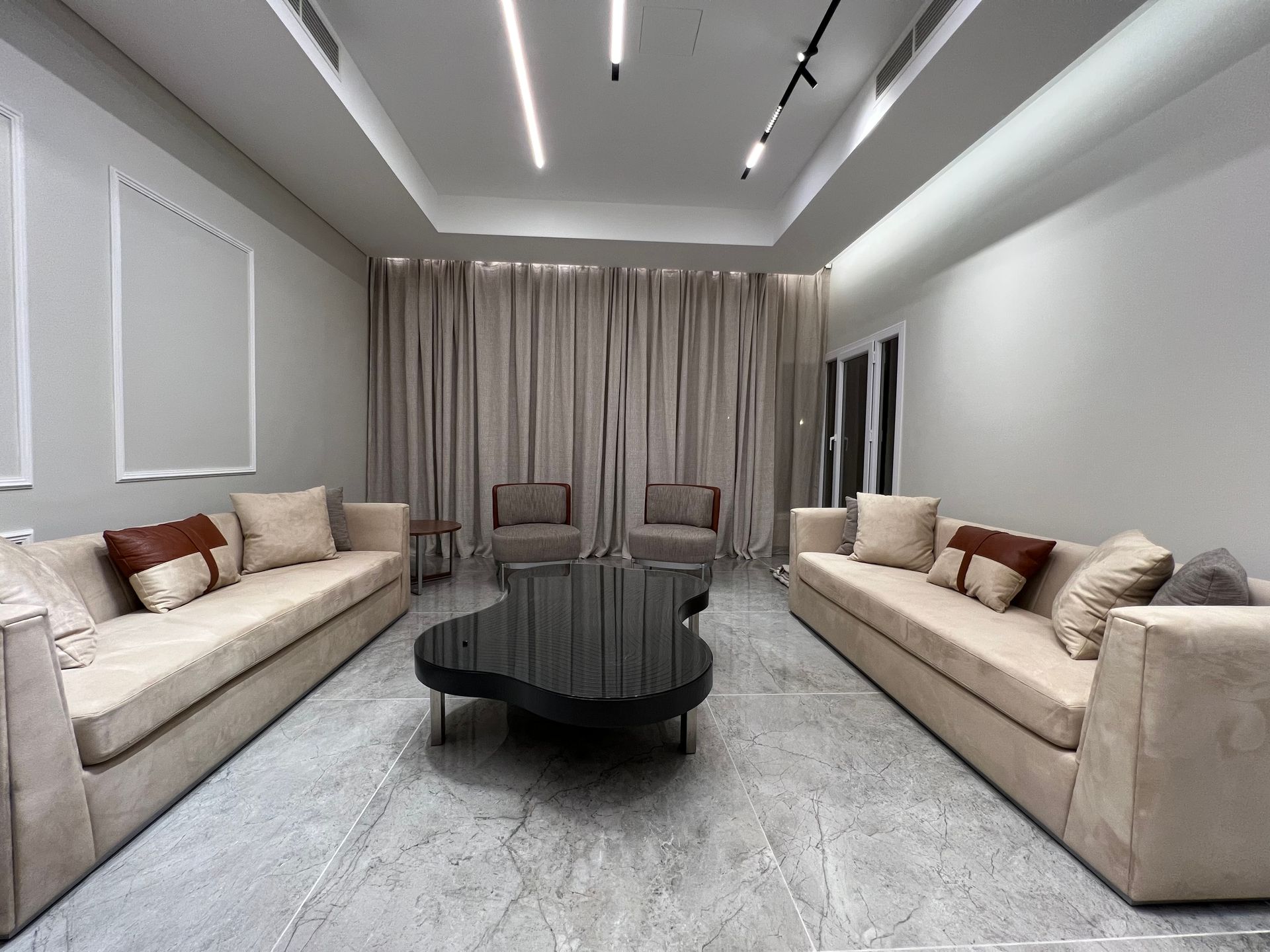 Modern living room with two beige sofas, two chairs, dark coffee table, and window.