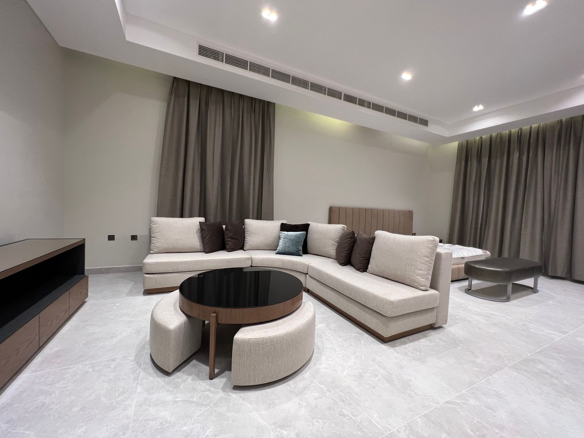 Modern living room with beige sectional sofa, dark wood coffee table, and neutral curtains.