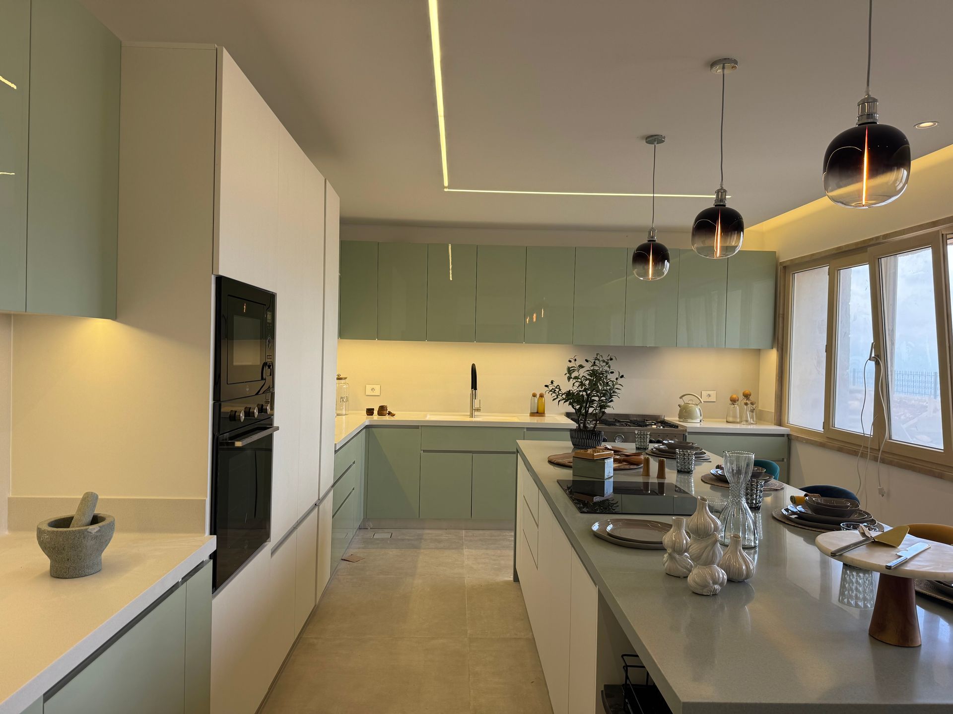Modern kitchen with sage cabinets, island, pendant lights, and white countertops.