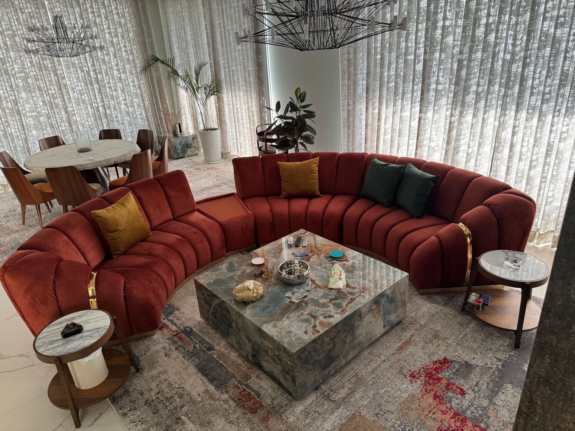 Curved red velvet sofa in luxury living room with marble coffee table, rugs, and round dining table.