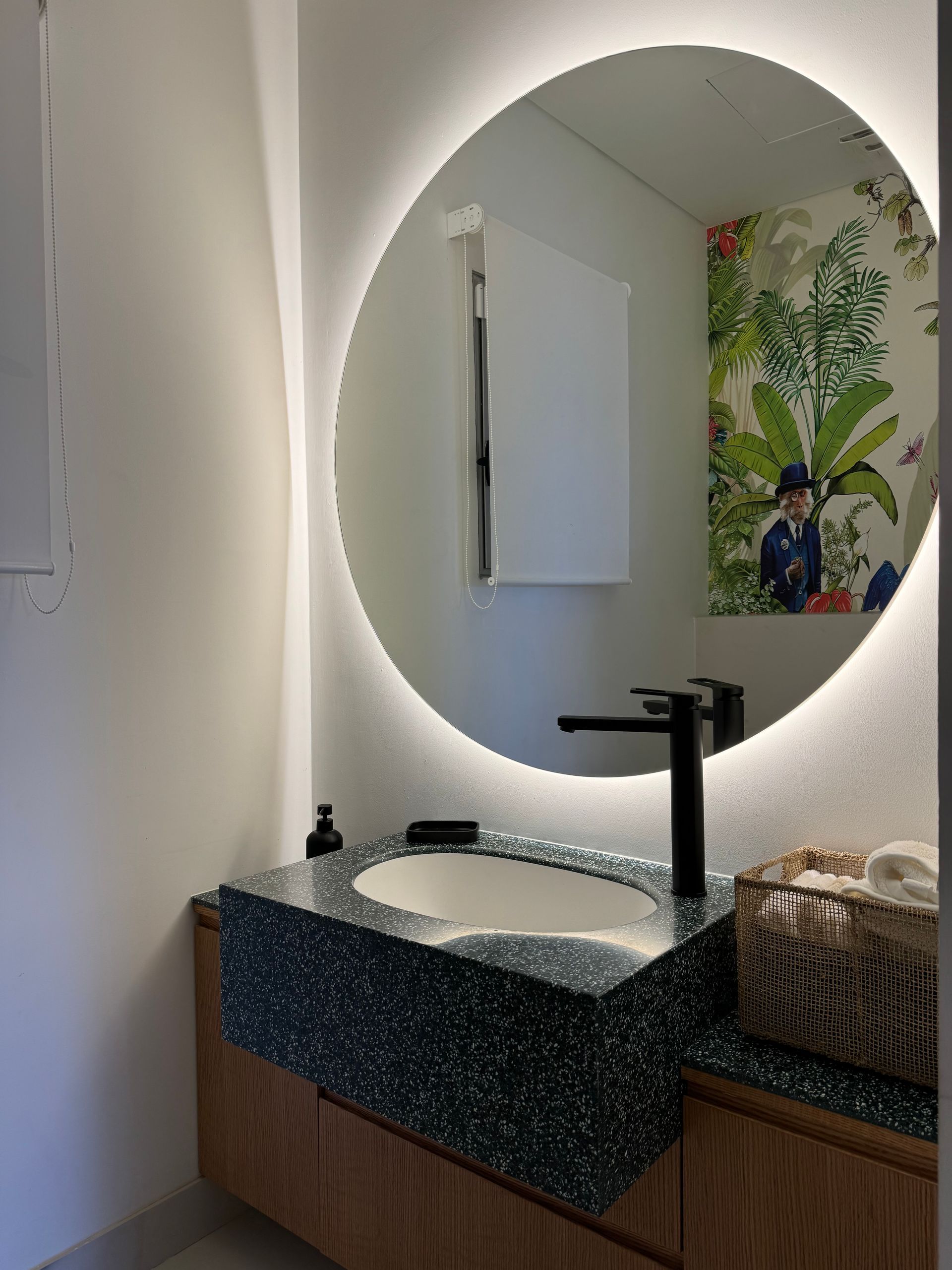 Bathroom with round mirror, backlit, above a sink with a black faucet and speckled countertop.