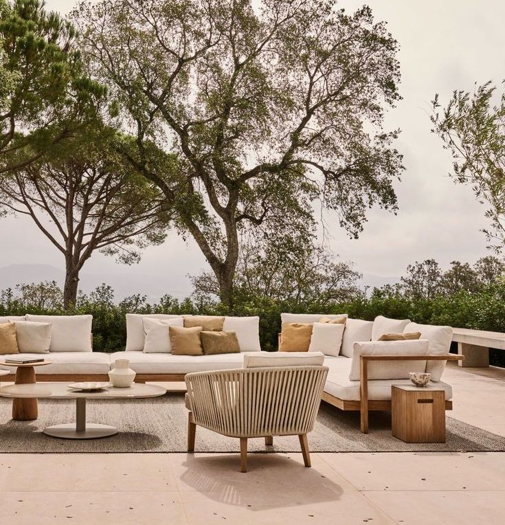 Outdoor patio with modern beige furniture, trees and a cloudy sky.