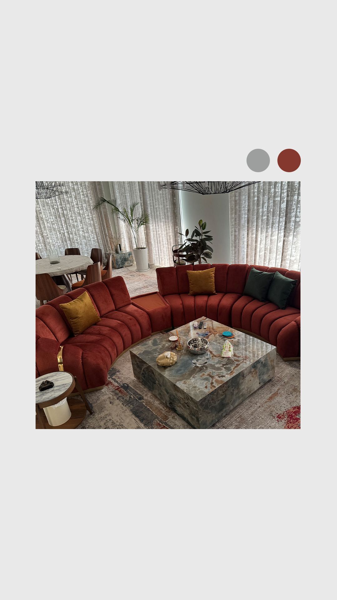 Living room with curved red sofa, marble coffee table, and colorful pillows.