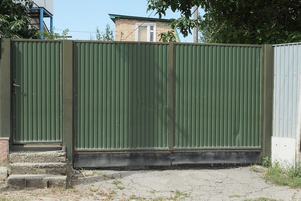 A Green Fence With a Gate in Front of a House — Perry's Timber & Fencing In Albion Park, NSW