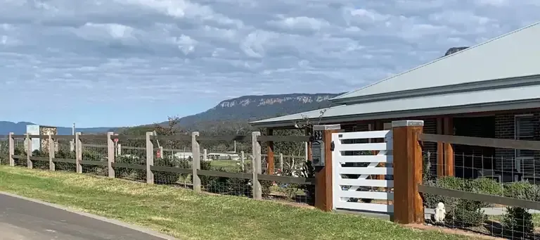 A Wooden Fence Surrounds A House With A Mountain In The Background — Perry's Timber & Fencing In Dapto, NSW