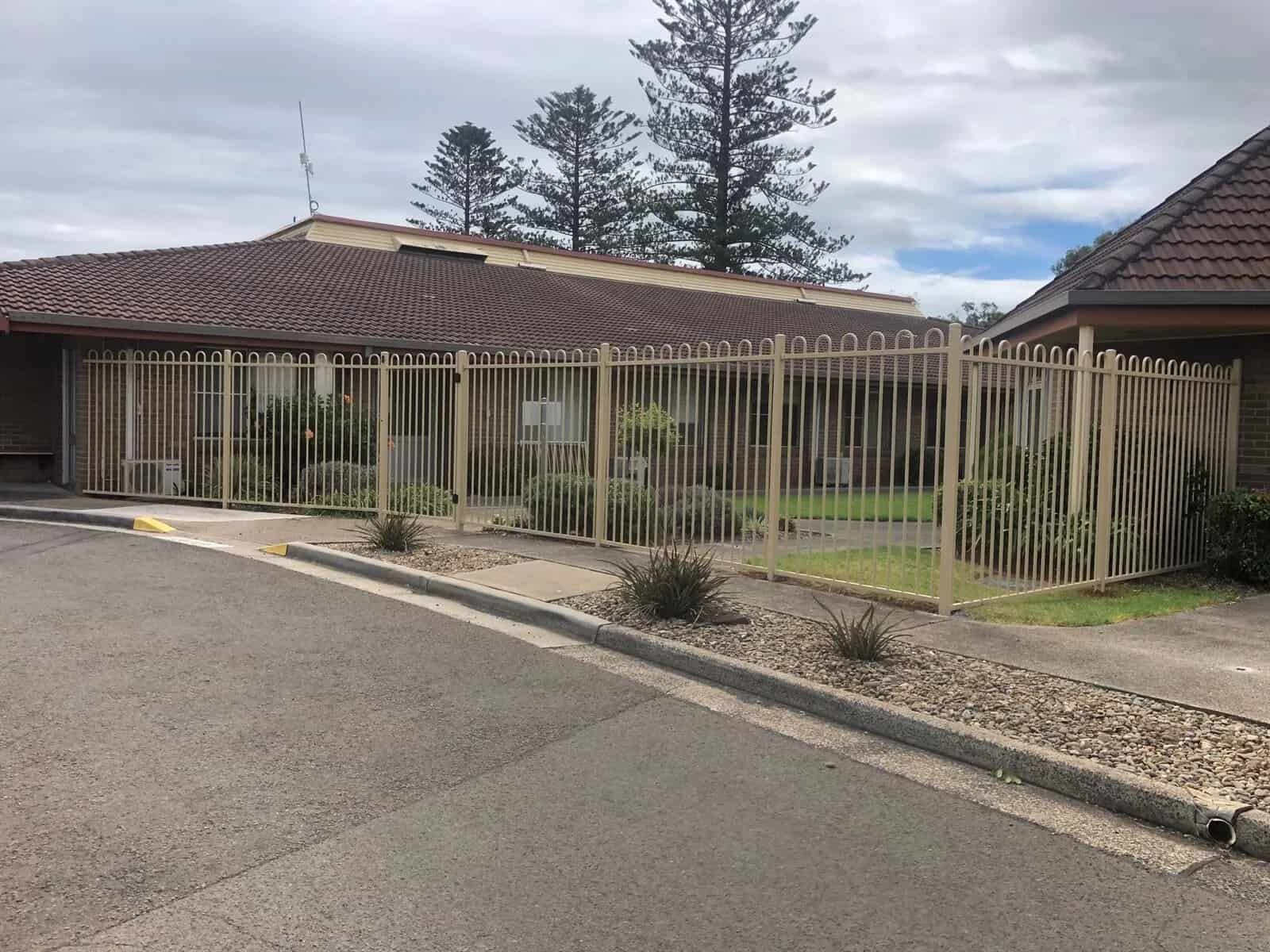 A House With A Fence Around It Is Sitting On The Side Of The Road — Perry's Timber & Fencing In Dapto, NSW