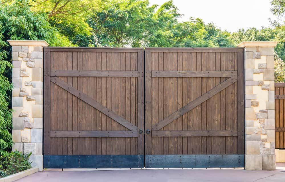 A Wooden Gate is Surrounded by Stone Pillars and Trees — Perry's Timber & Fencing In Dapto, NSW