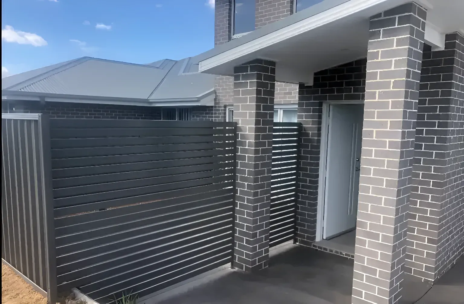 A Brick House With A Black Fence And A White Door — Perry's Timber & Fencing In Dapto, NSW