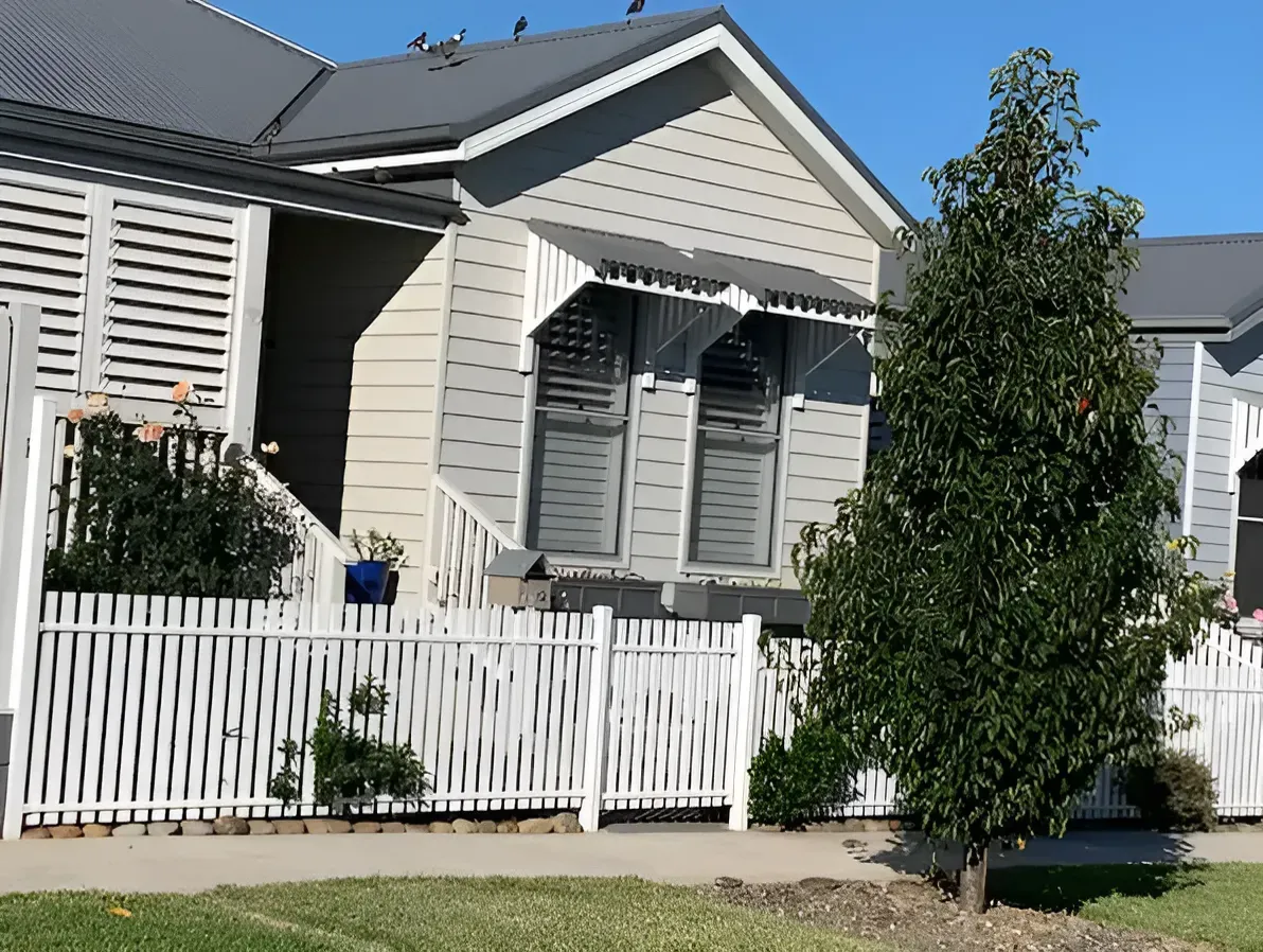 A House With A White Picket Fence And A Tree In Front Of It — Perry's Timber & Fencing In Dapto, NSW
