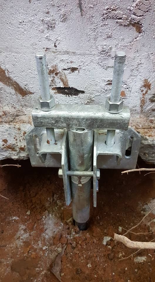 Metal bracket and anchor installed in soil against a concrete wall for structural support.