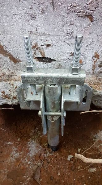 Metal bracket and anchor installed in soil against a concrete wall for structural support.