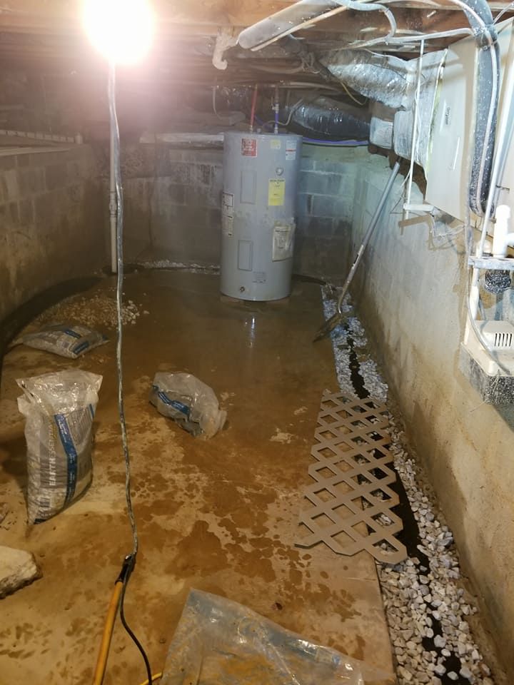 Flooded crawl space with water heater, plastic latticework, and clear plastic bags.