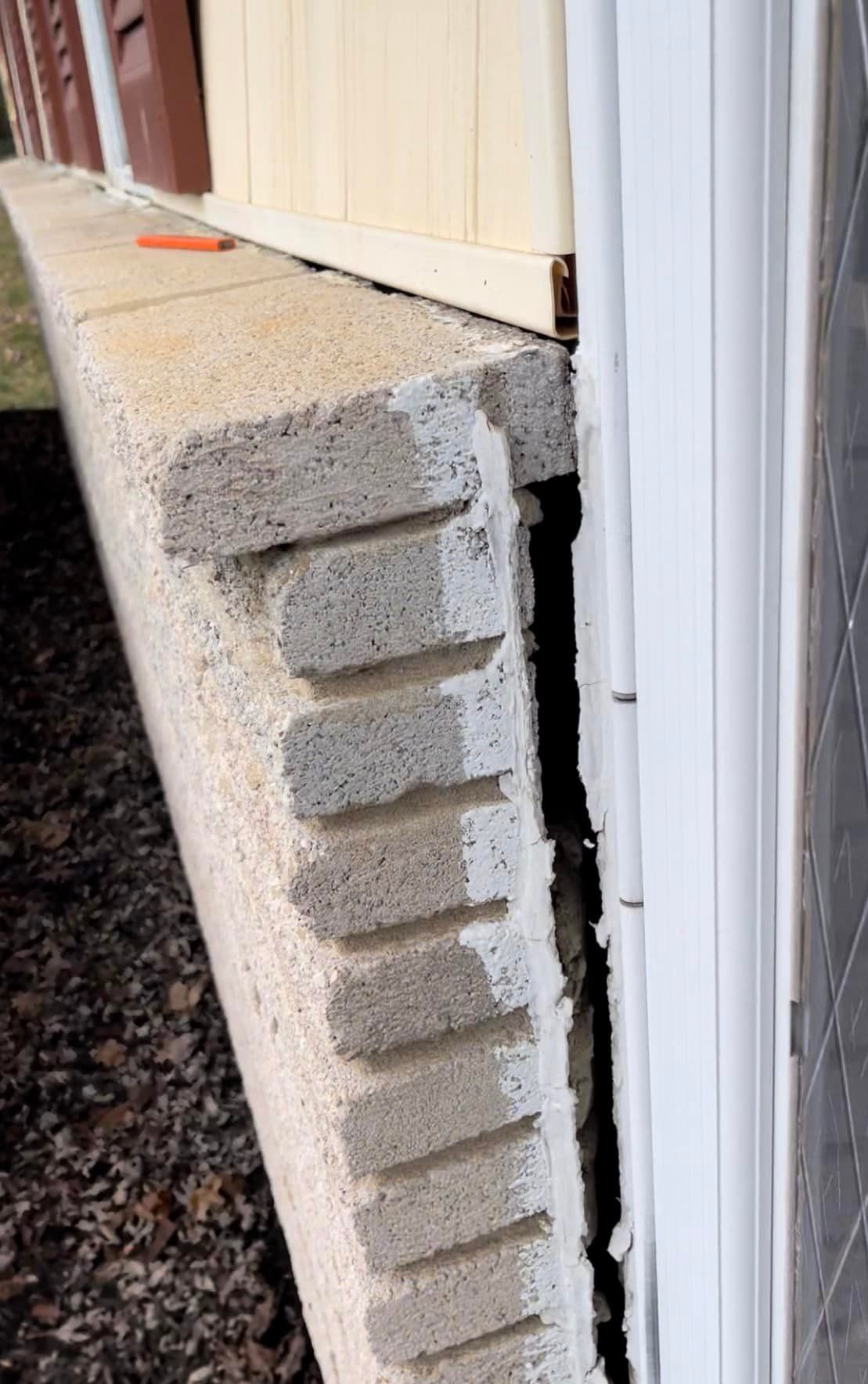 Damaged cinder block foundation next to white trim and a light yellow wall. The blocks show cracks and separation.