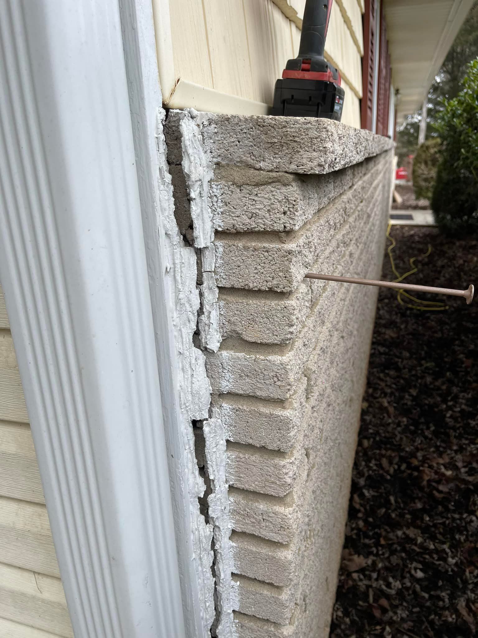 A brick wall with a nail sticking out; an electric drill is above the wall.