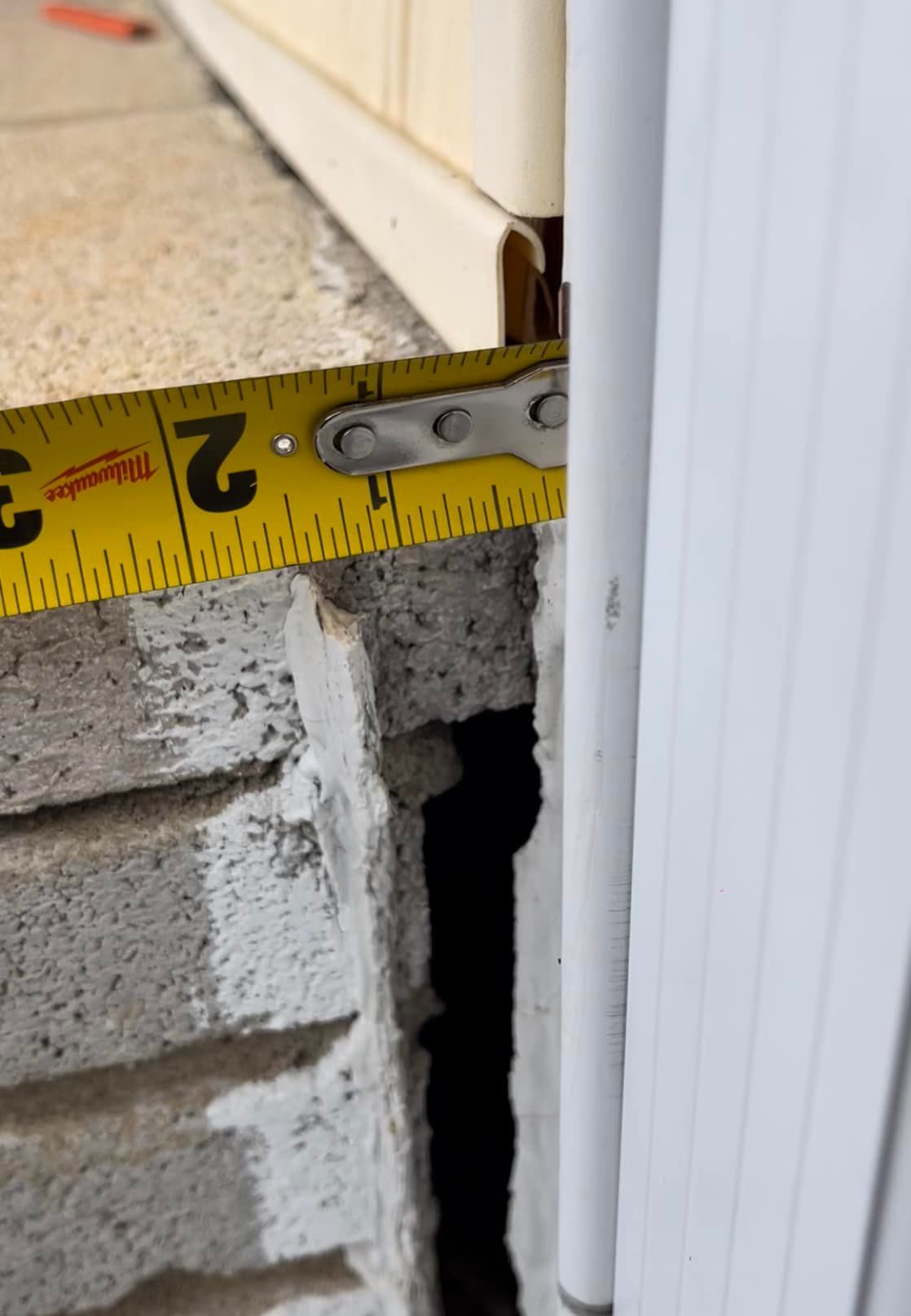 A tape measure shows a 2-inch gap between a brick wall and a white door frame.