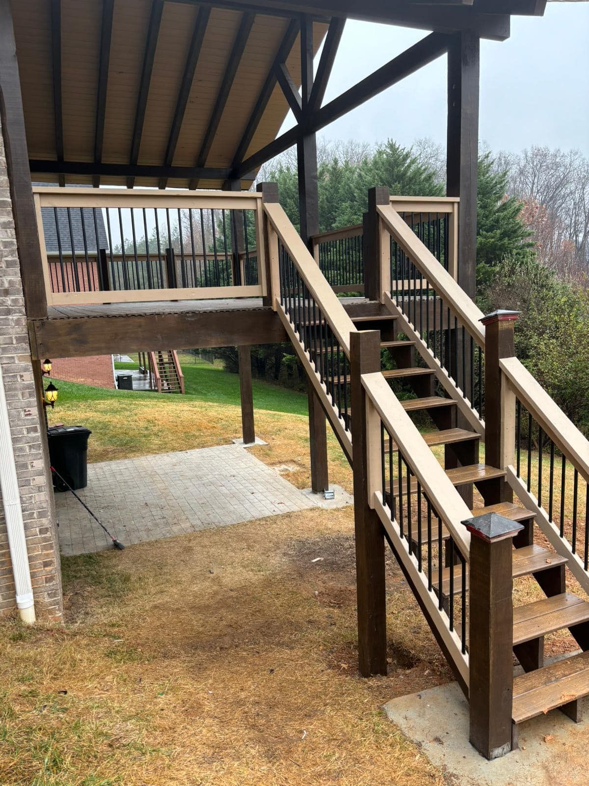 Deck with stairs and railing, dark brown with tan accents, brick building, overcast outdoors.