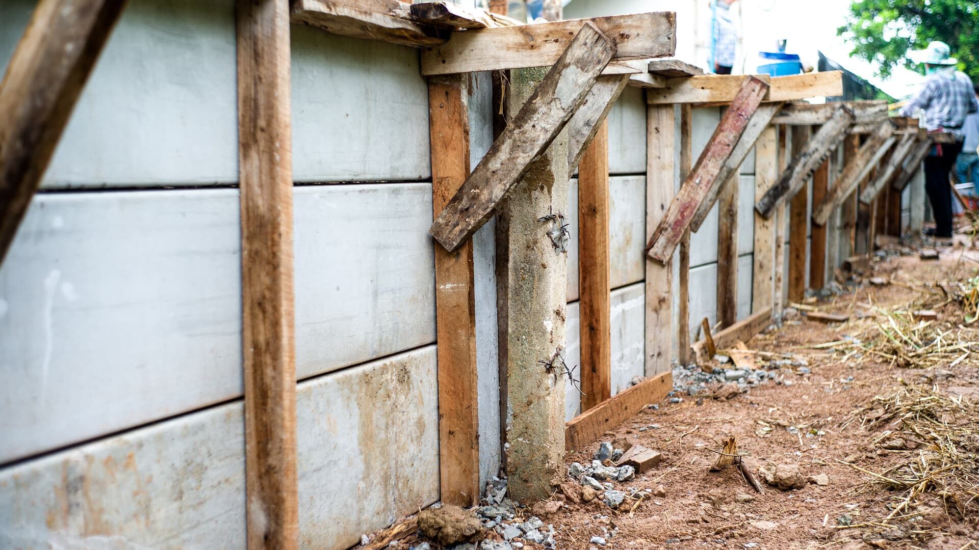 Concrete wall under construction, supported by wooden framing and bracing. Outdoors.