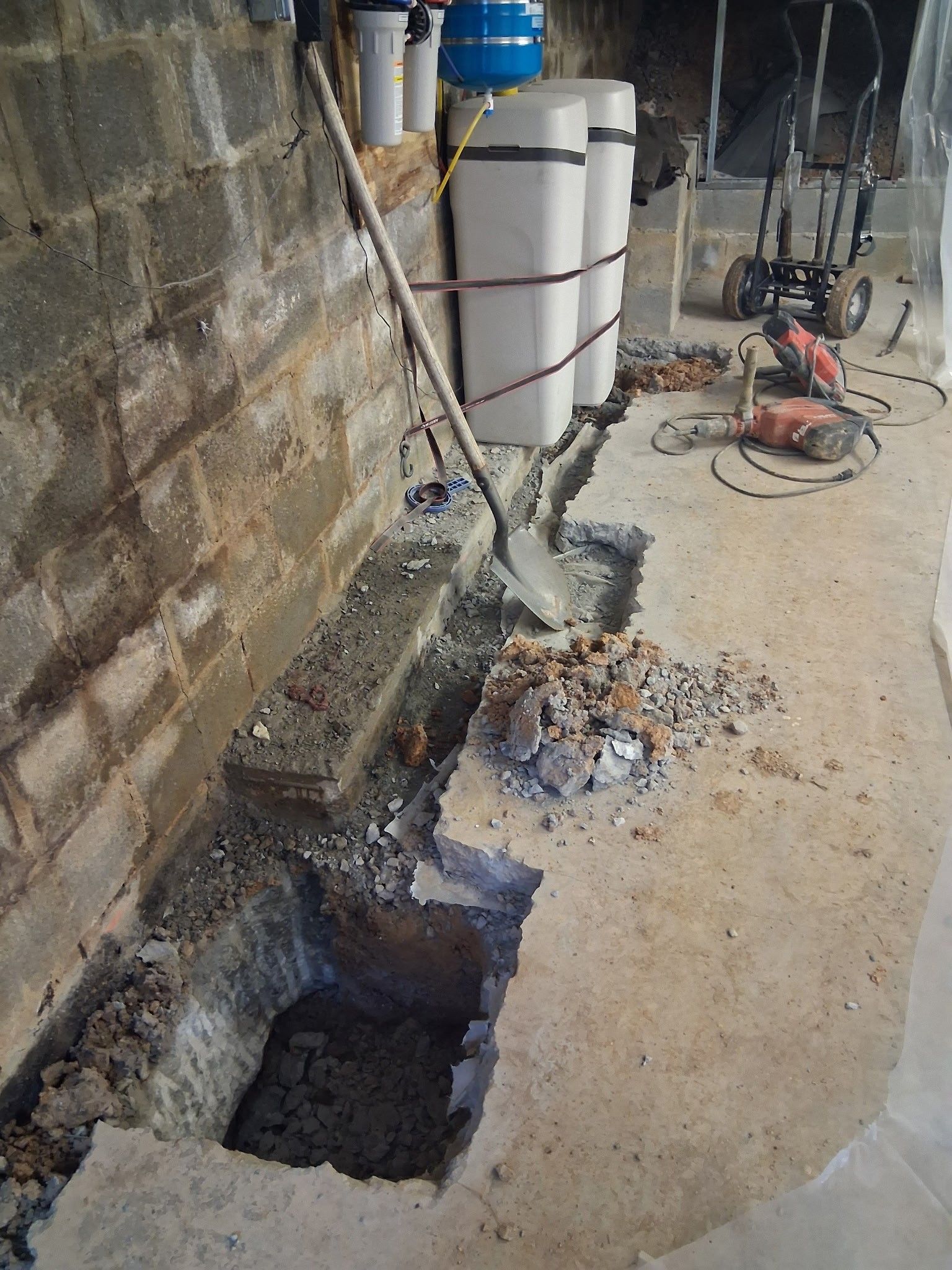 Basement floor repair: A shovel rests in a concrete trench. A jackhammer sits nearby.
