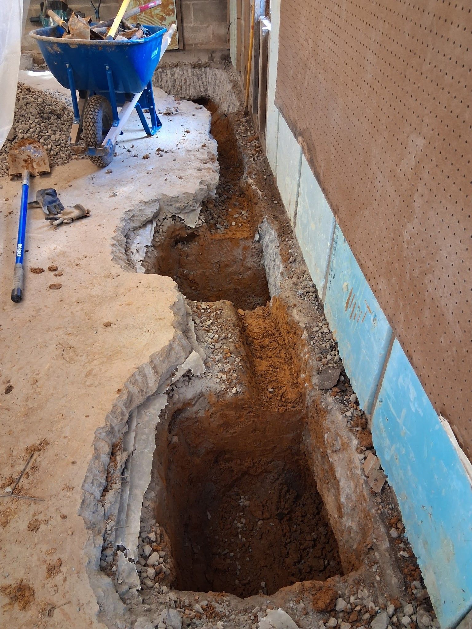 Exterior wall renovation: Gray panels installed below brick wall, with gravel and construction materials present.
