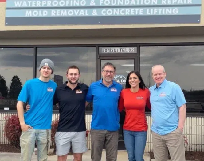 Five people stand outside a business, posing for a photo. Sign above reads 