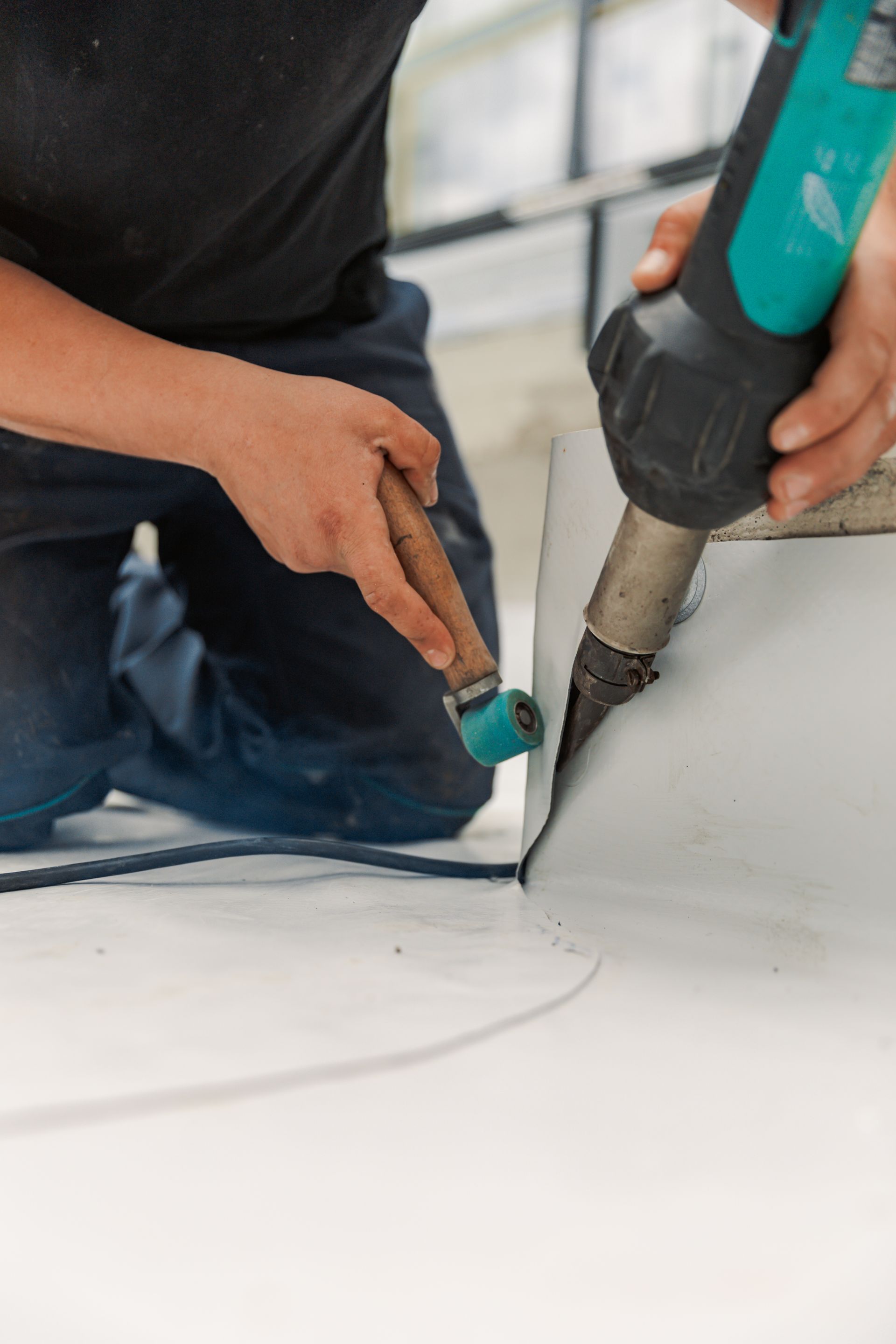 Person using a heat gun to weld a white membrane on a rooftop.
