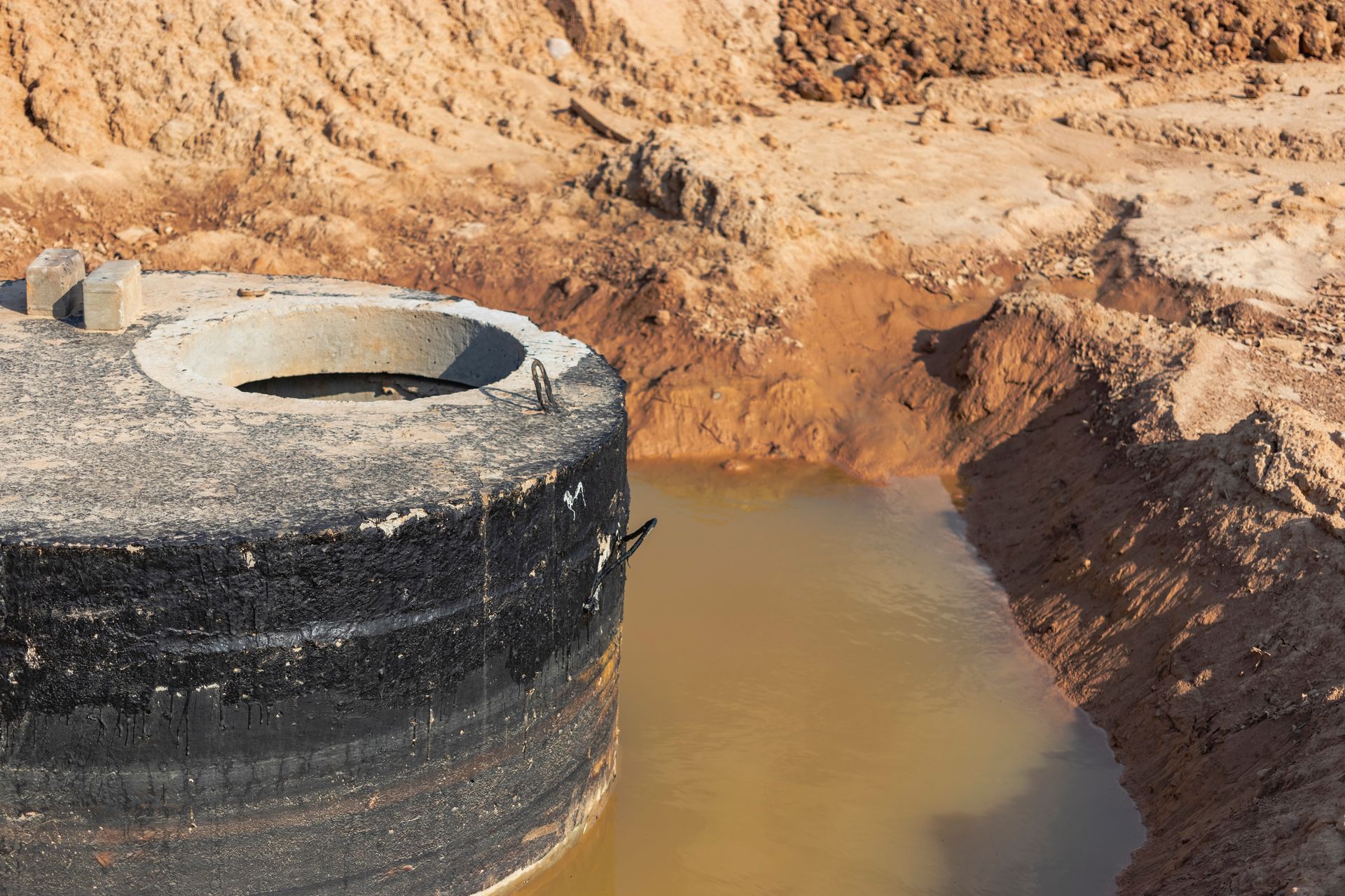 Concrete well ring in muddy water within an excavated area, with earthen walls.