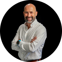 A bald man with a beard is standing with his arms crossed and smiling.