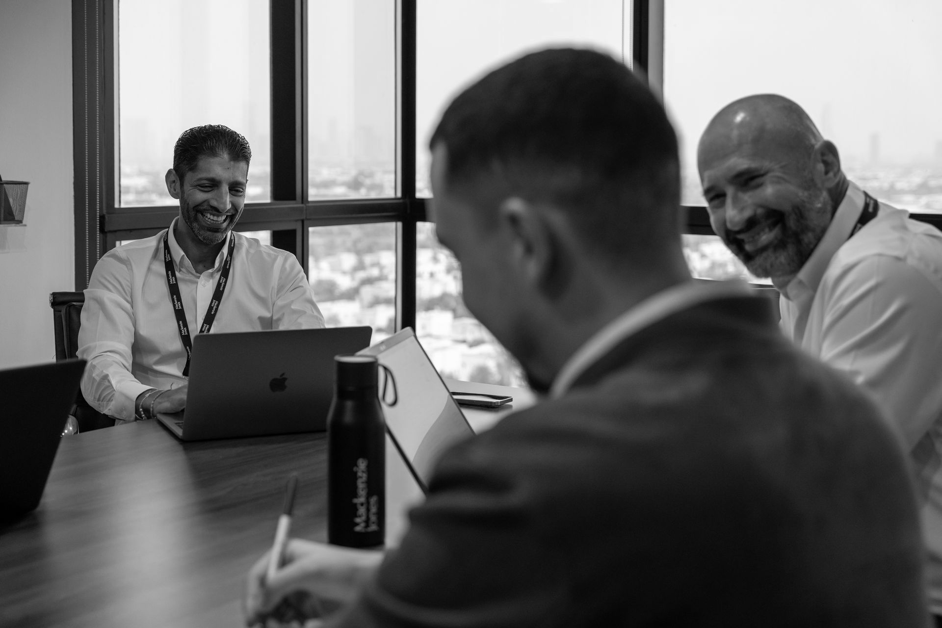 A group of people are sitting around a table with laptops.