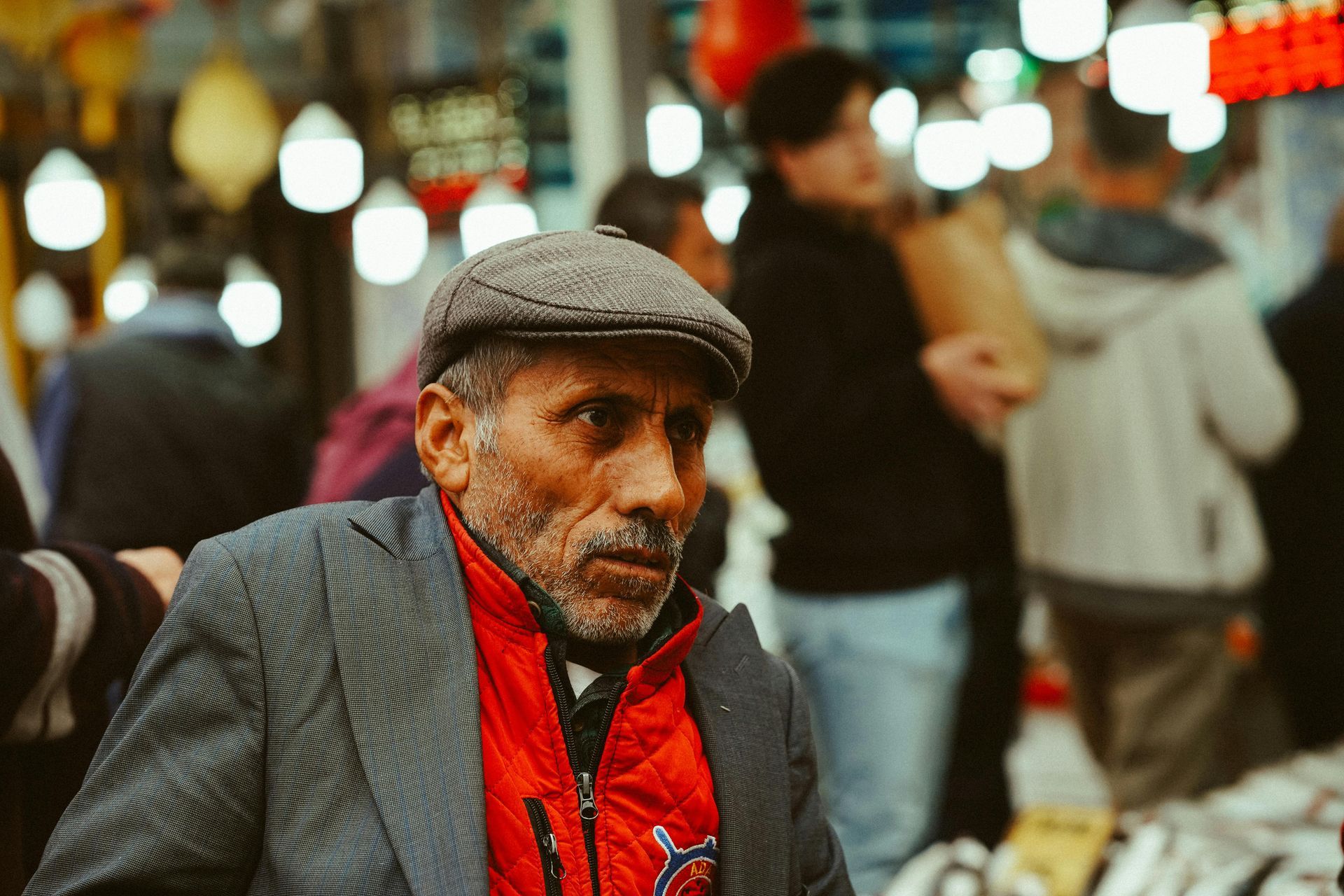 A man in a suit and hat is sitting in a crowded market.