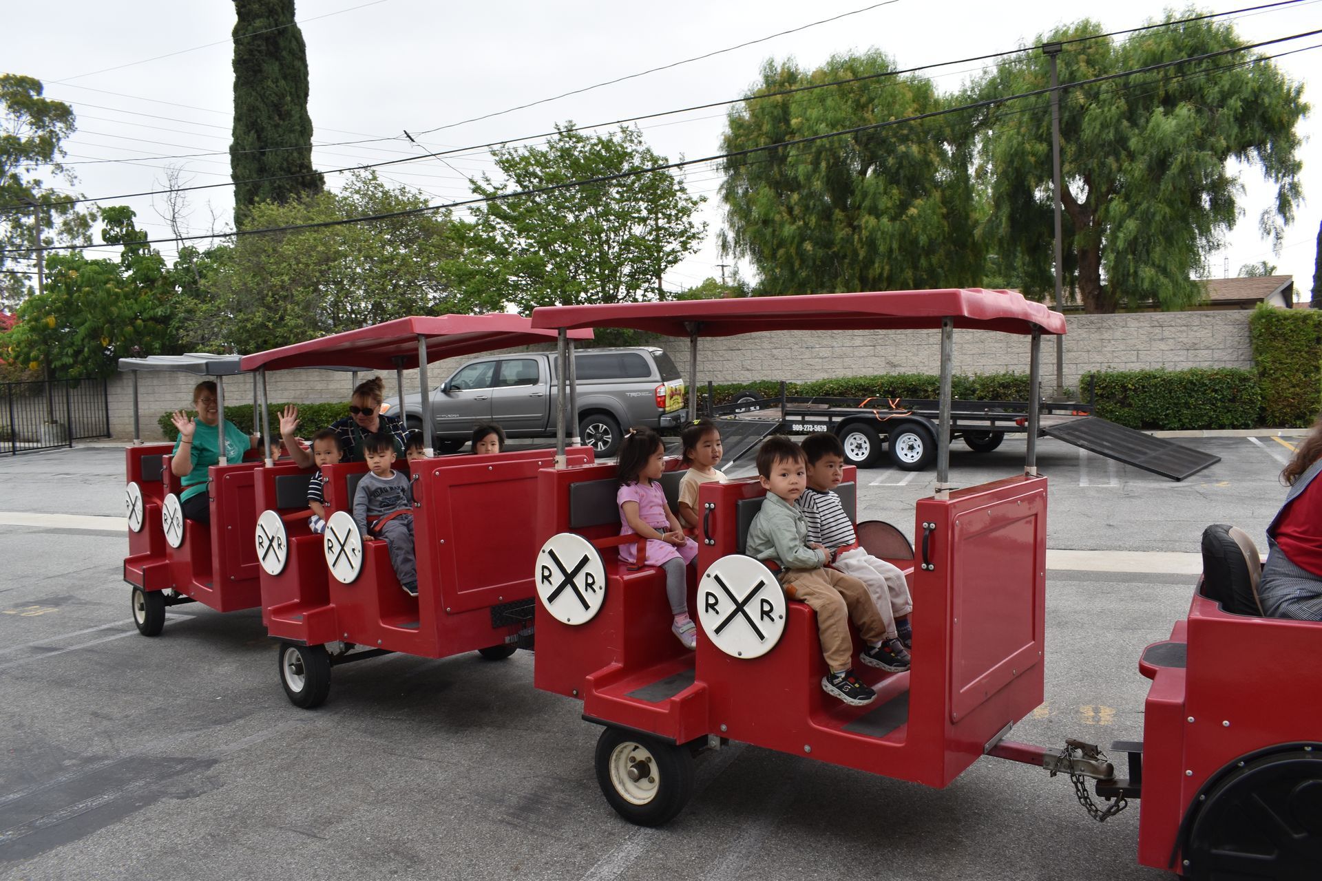 Children riding a red train on wheels outdoors. They are smiling.