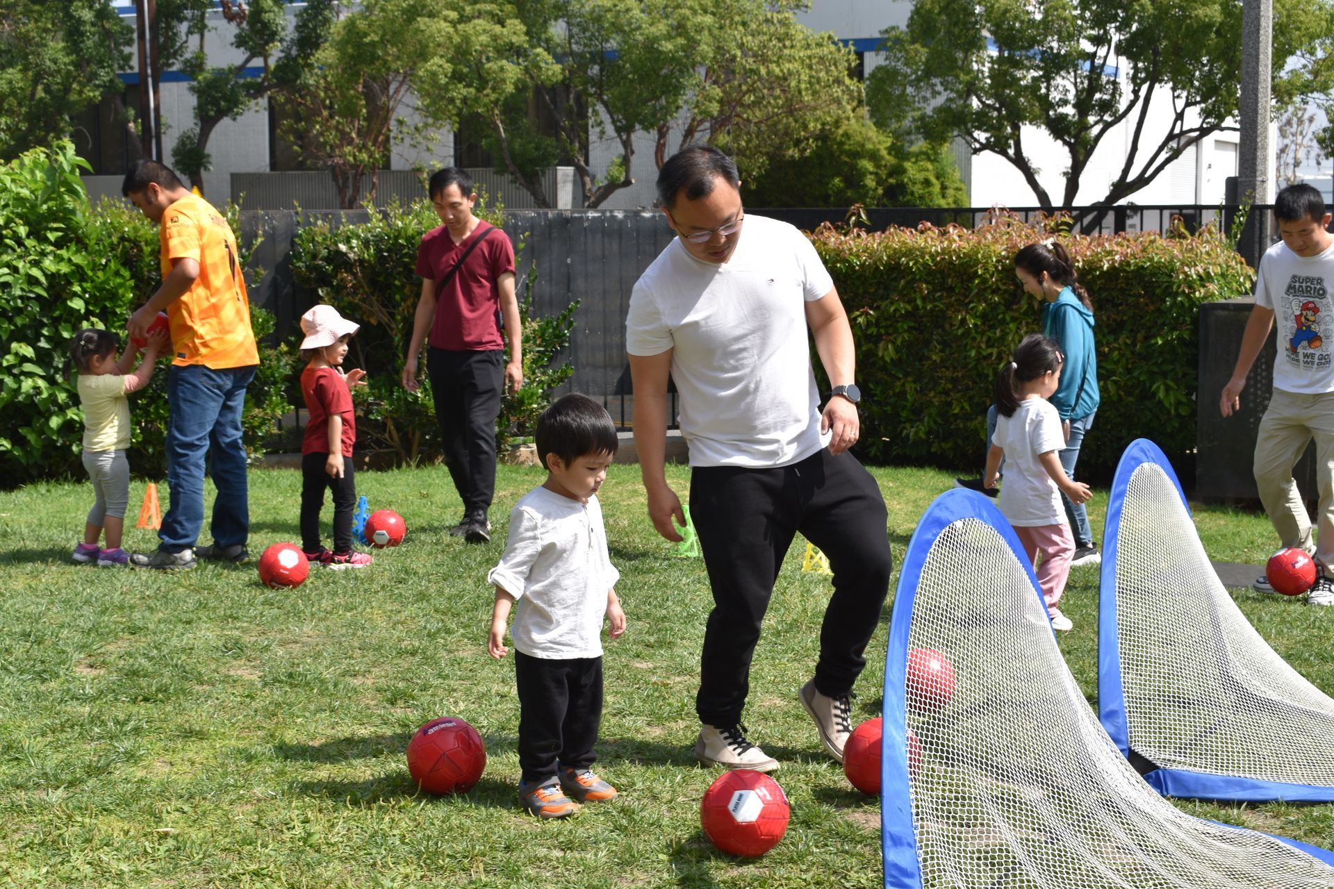 People and kids playing soccer outdoors.