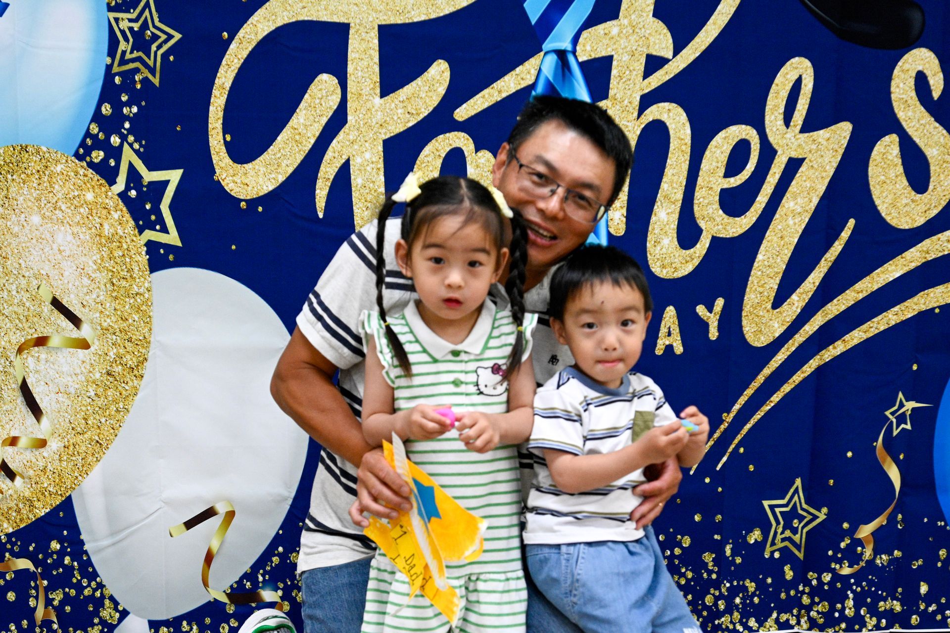 Father with two young children posing in front of a Father's Day backdrop.