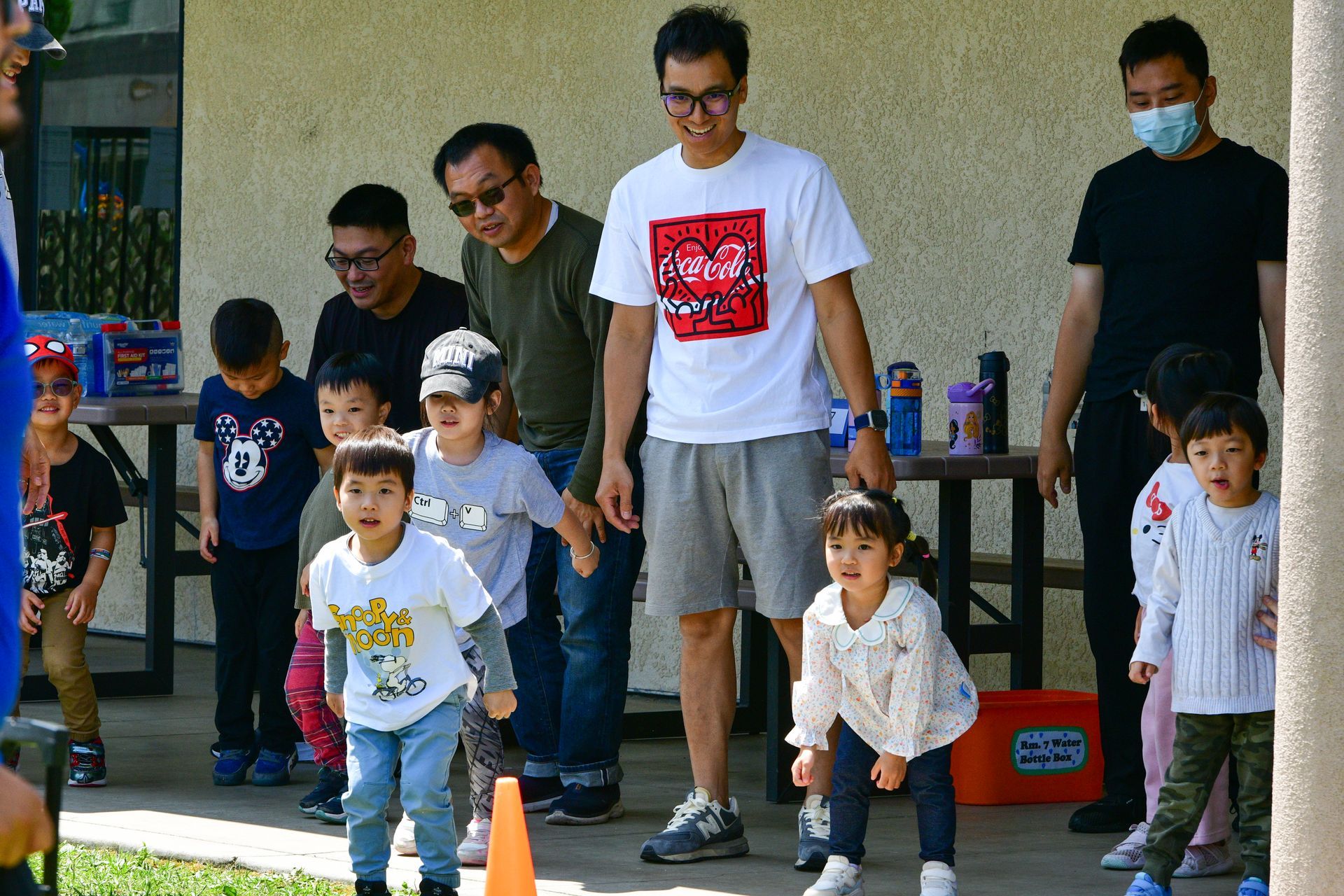 Children and adults at an outdoor event. Kids in a line, ready to run with adults watching.