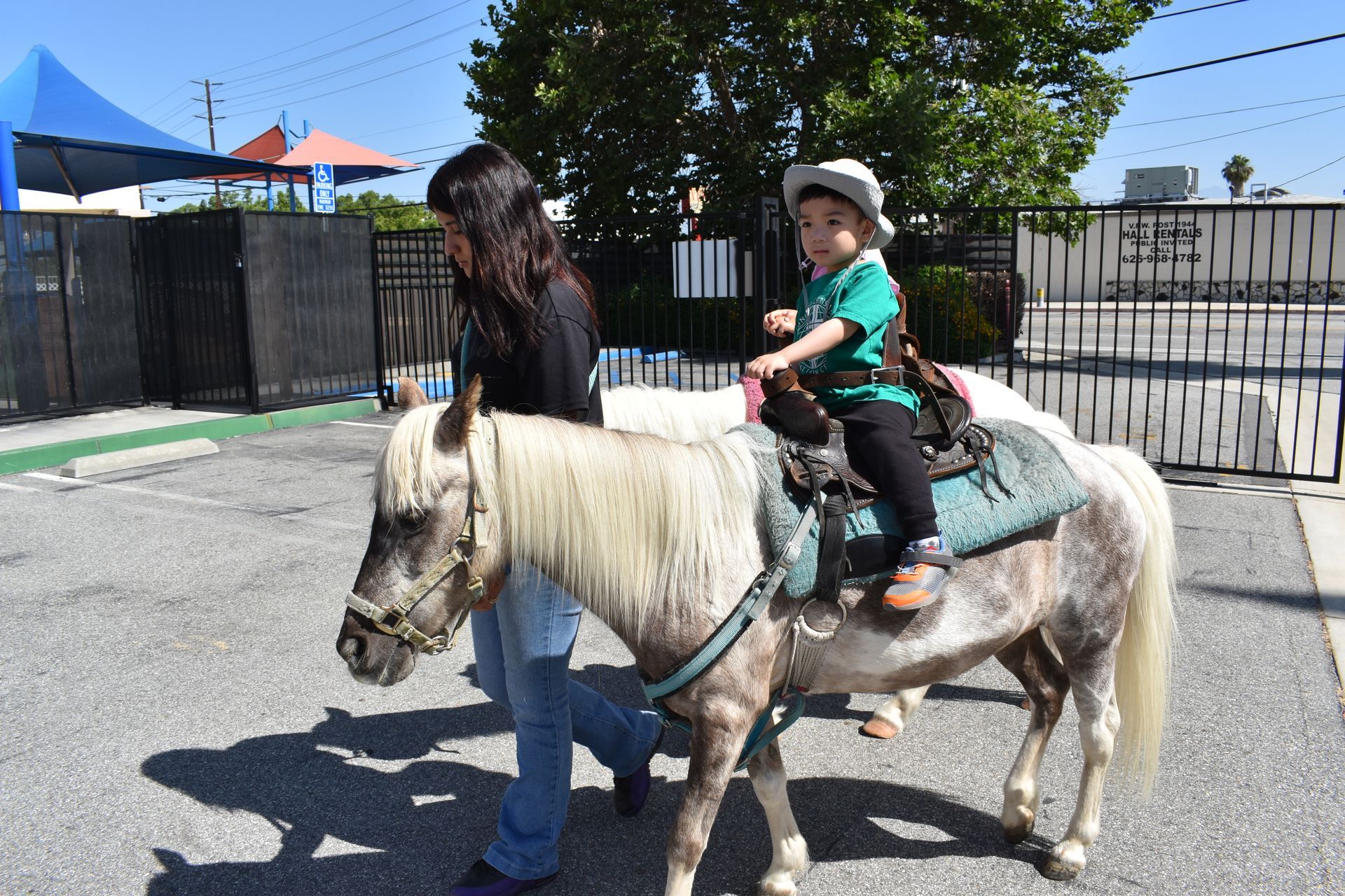 A child rides a pony, led by an adult on a sunny day.