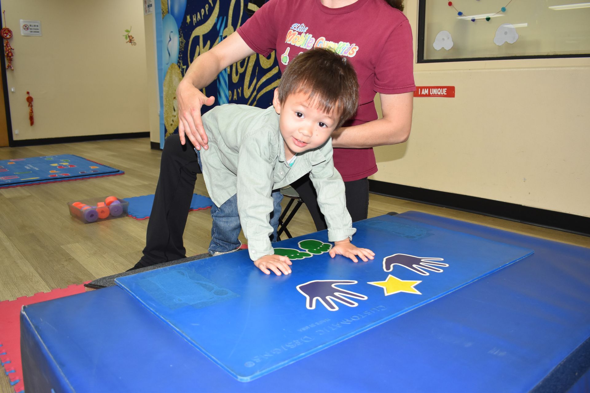 Child crawling on blue mat with adult assistance; indoor setting.