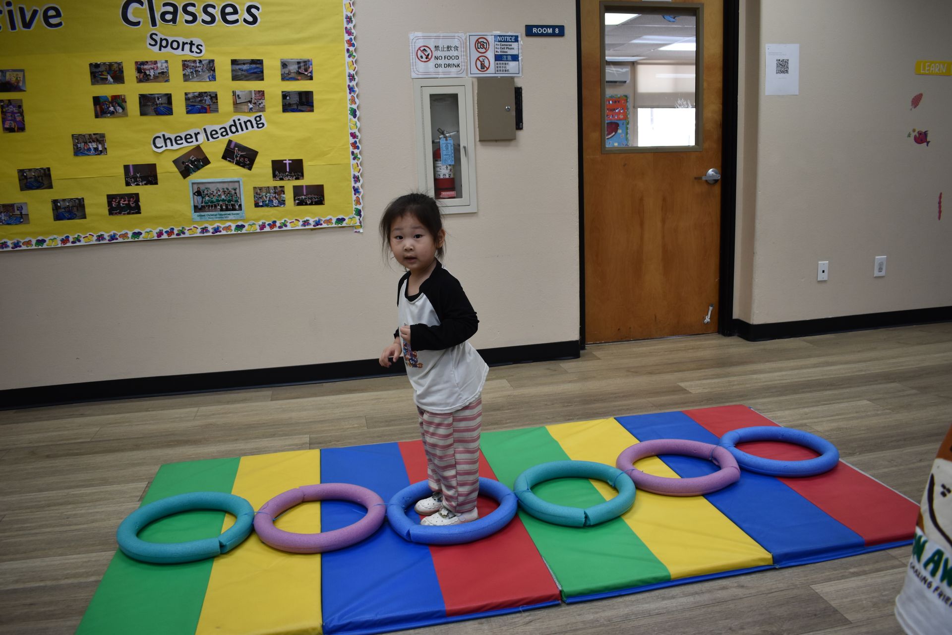 Girl balancing on colorful rings on a mat in a classroom.