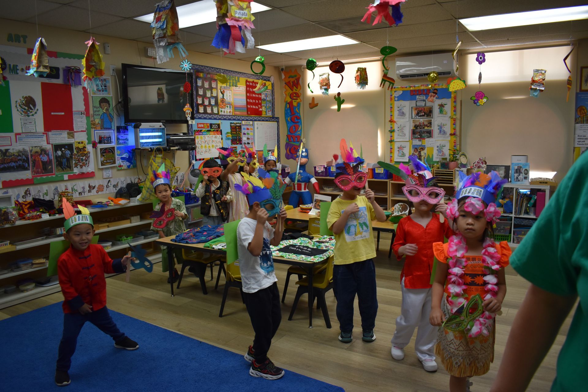 Children wearing party hats and leis dance in a decorated classroom.